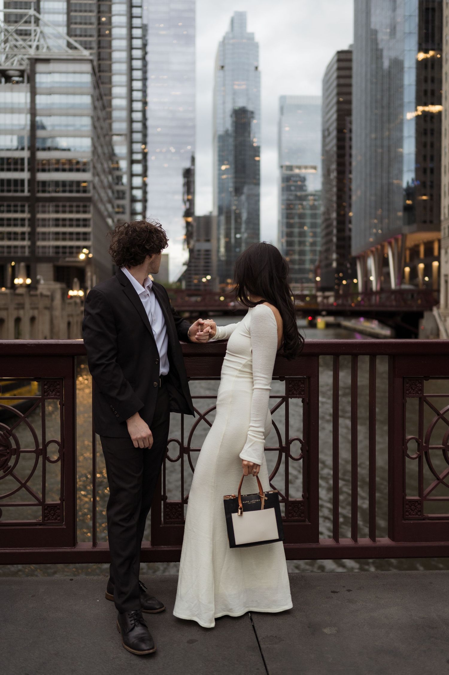 Couple holding hands on a bridge with Chicago city skyline in the background during their engagement shoot.