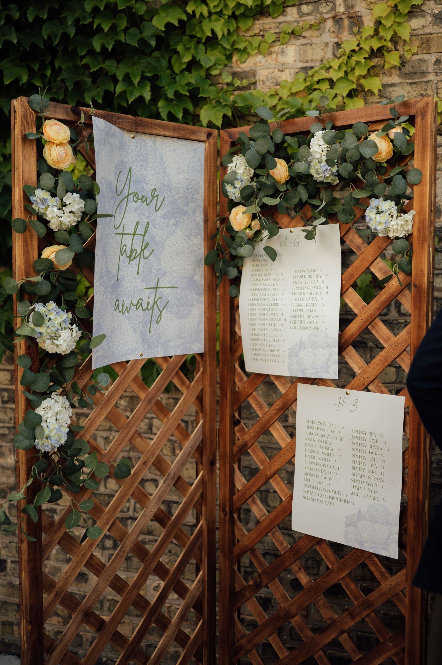 Wooden lattice wedding seating chart display adorned with white hydrangeas, eucalyptus, and yellow roses.