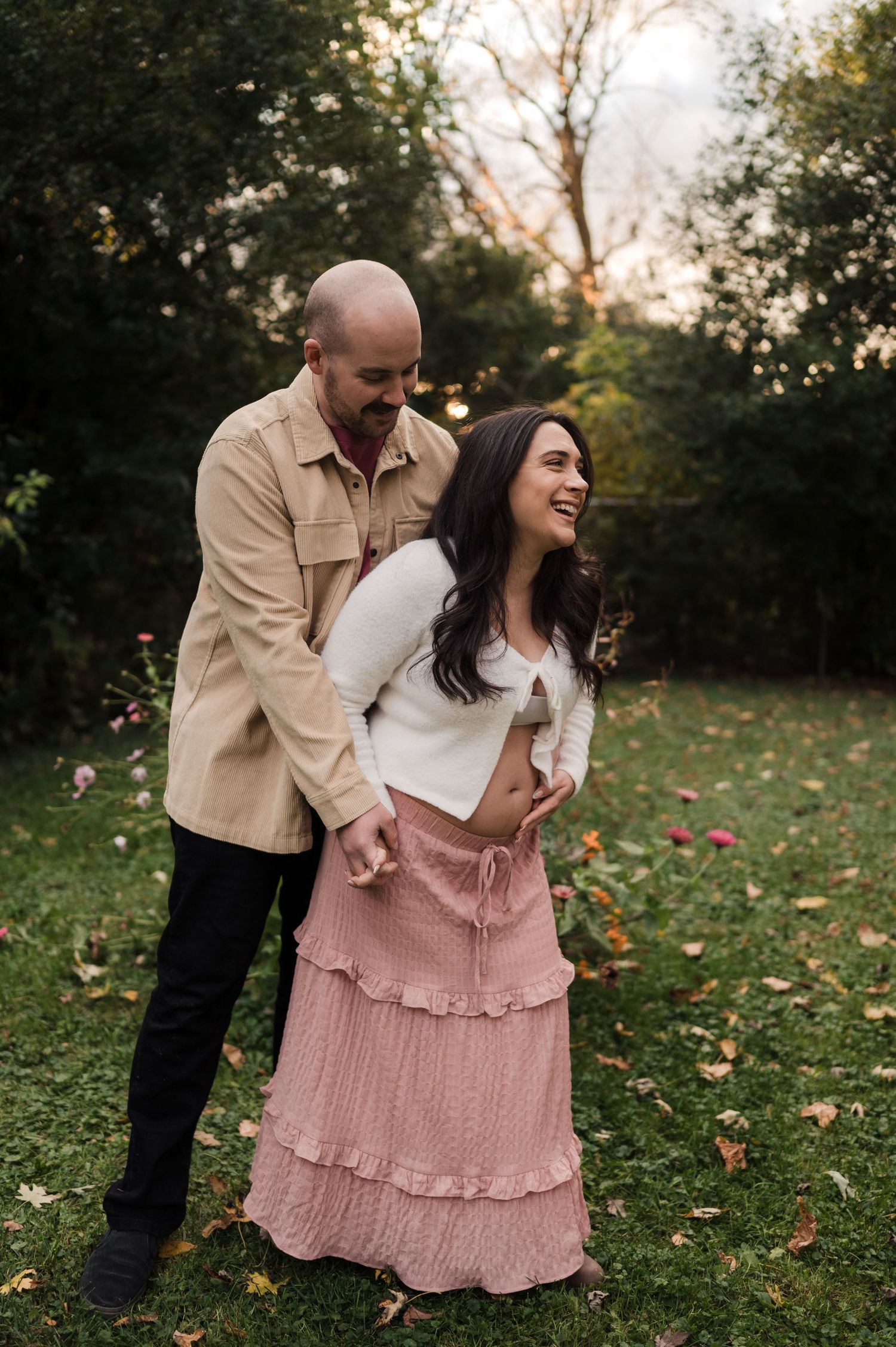 Couple laughing together in autumn park, woman in pink maxi skirt and white top, man in beige shirt.