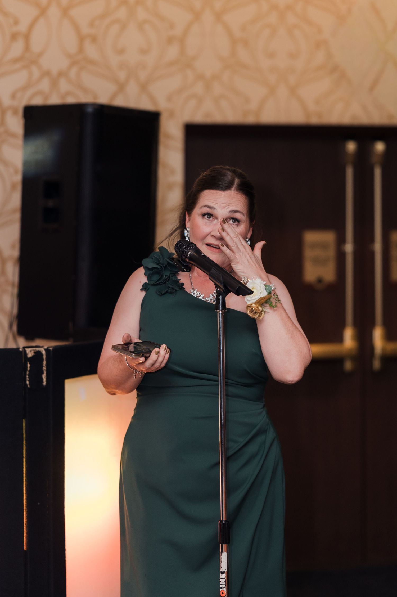 A performer in a dark green shirt gestures emotively while speaking into a microphone on stage.