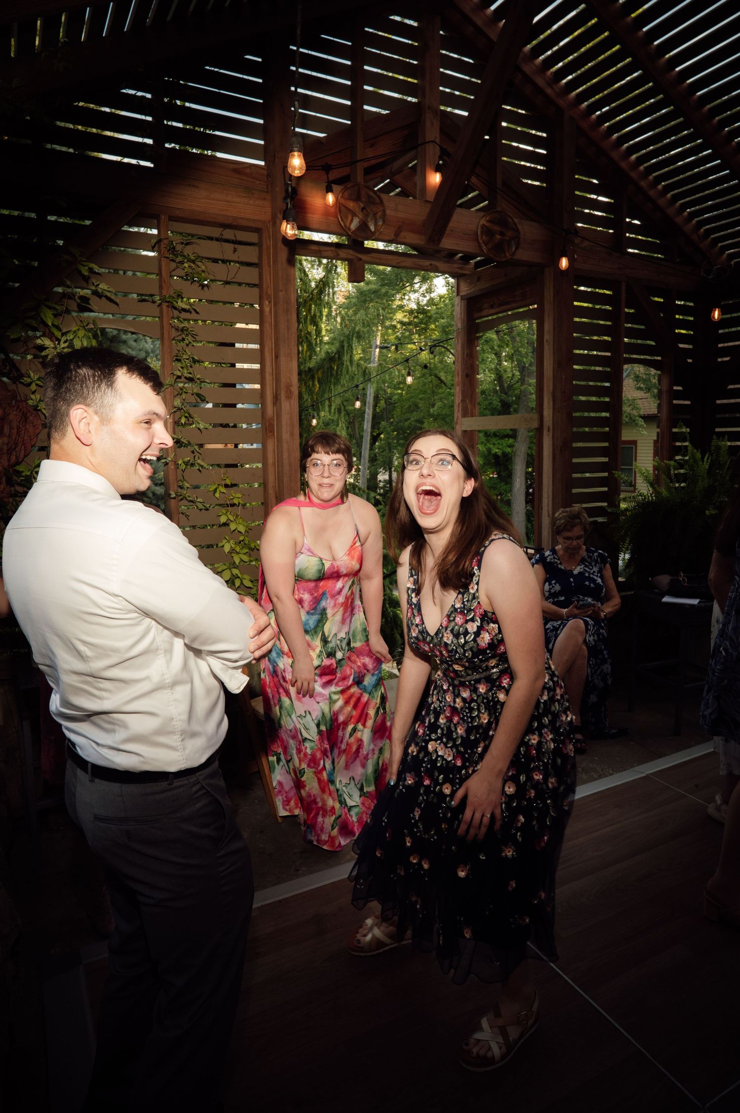 Guests laughing and dancing at a tropical wedding reception venue with wooden slat walls and string lights.