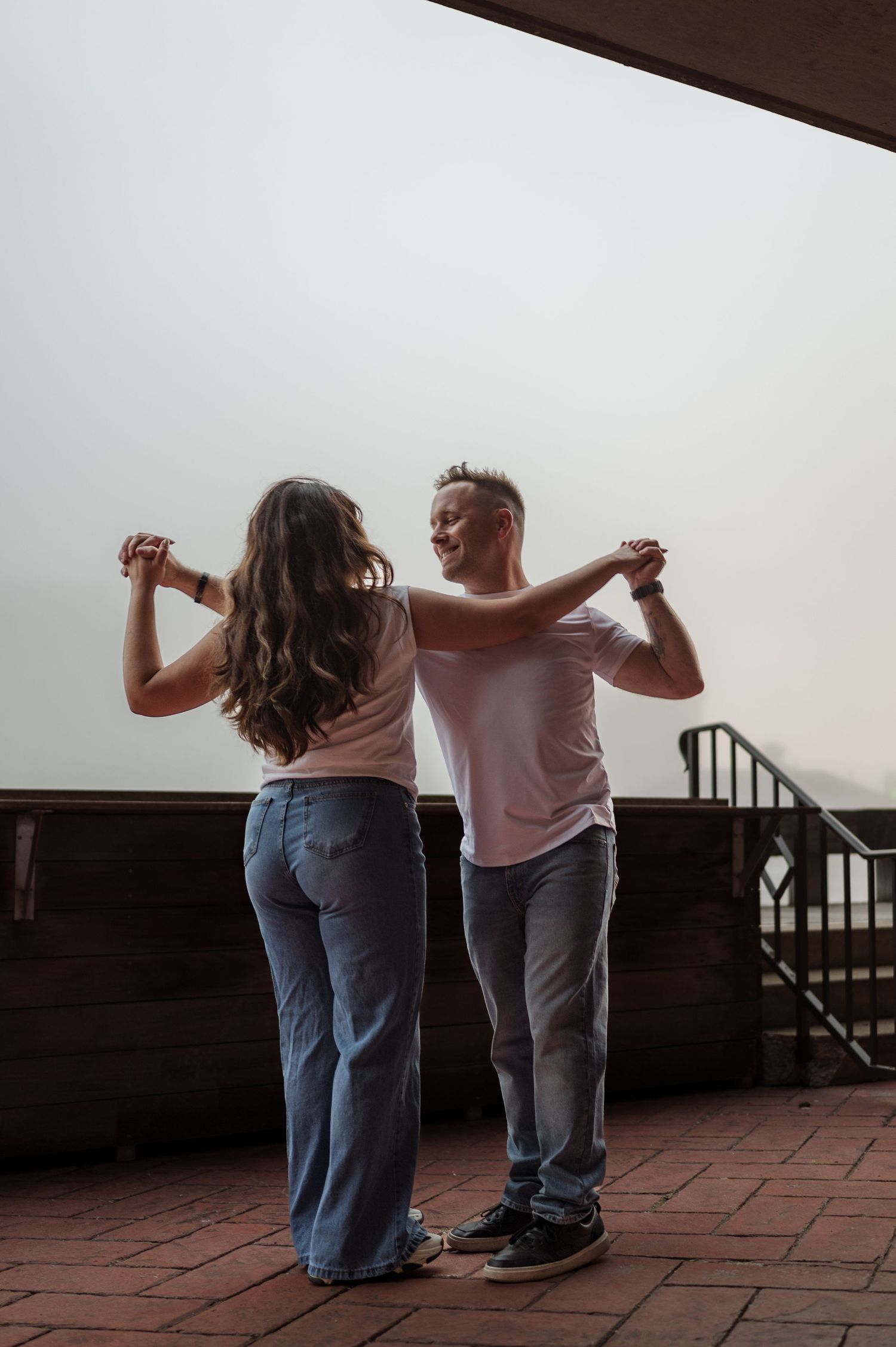 A couple dances together at sunset on a brick terrace, both wearing casual outfits in muted tones.