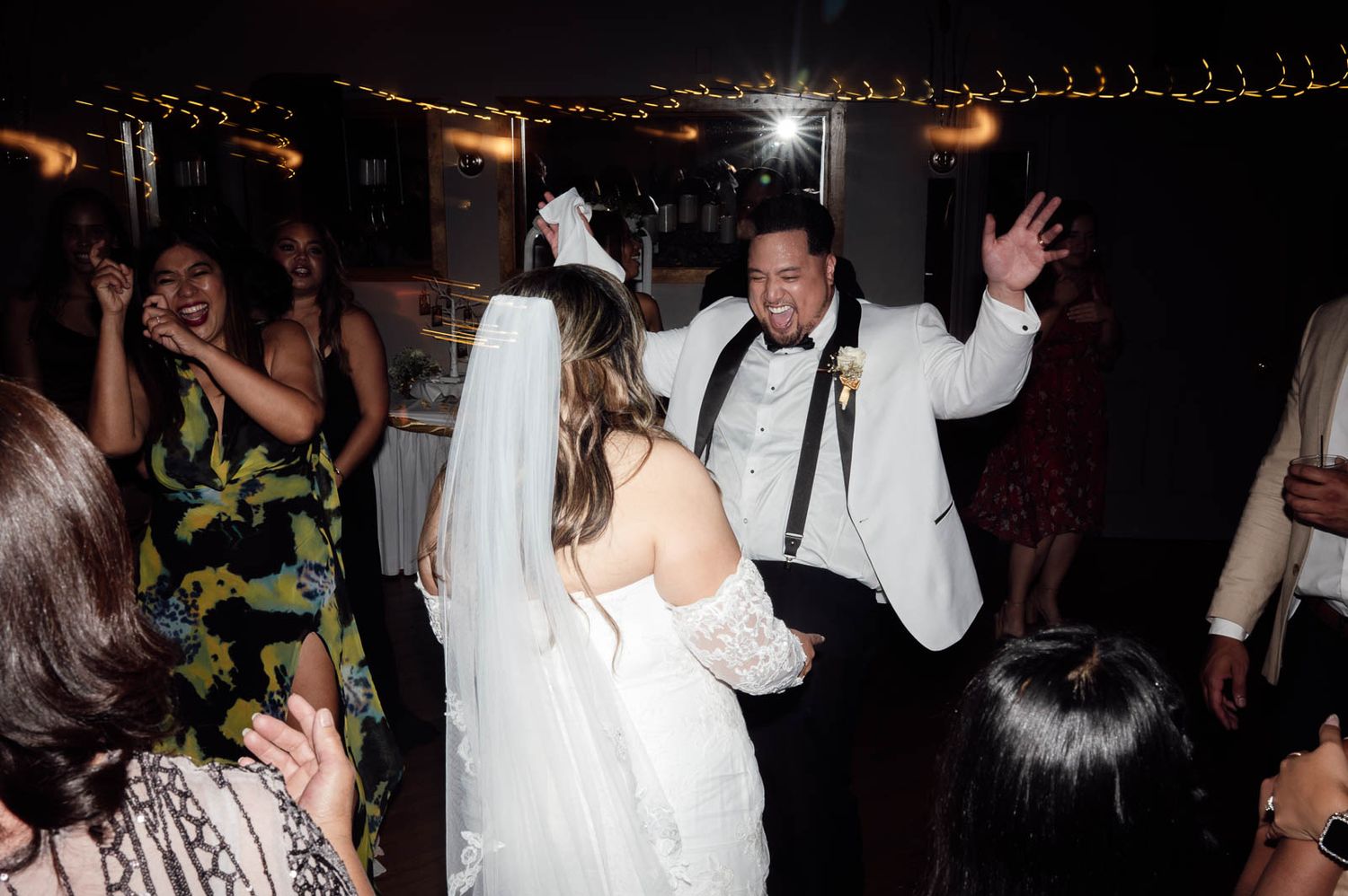 Bride and groom dancing joyfully with guests at lively indoor wedding reception.