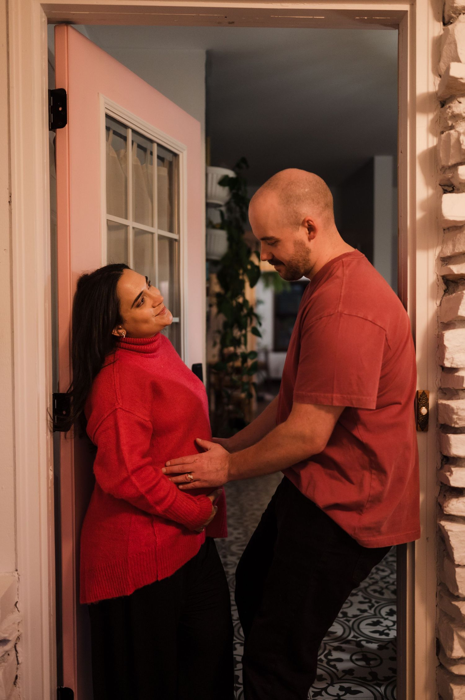 Expecting couple in matching red outfits sharing intimate moment in doorway, man cradling baby bump.