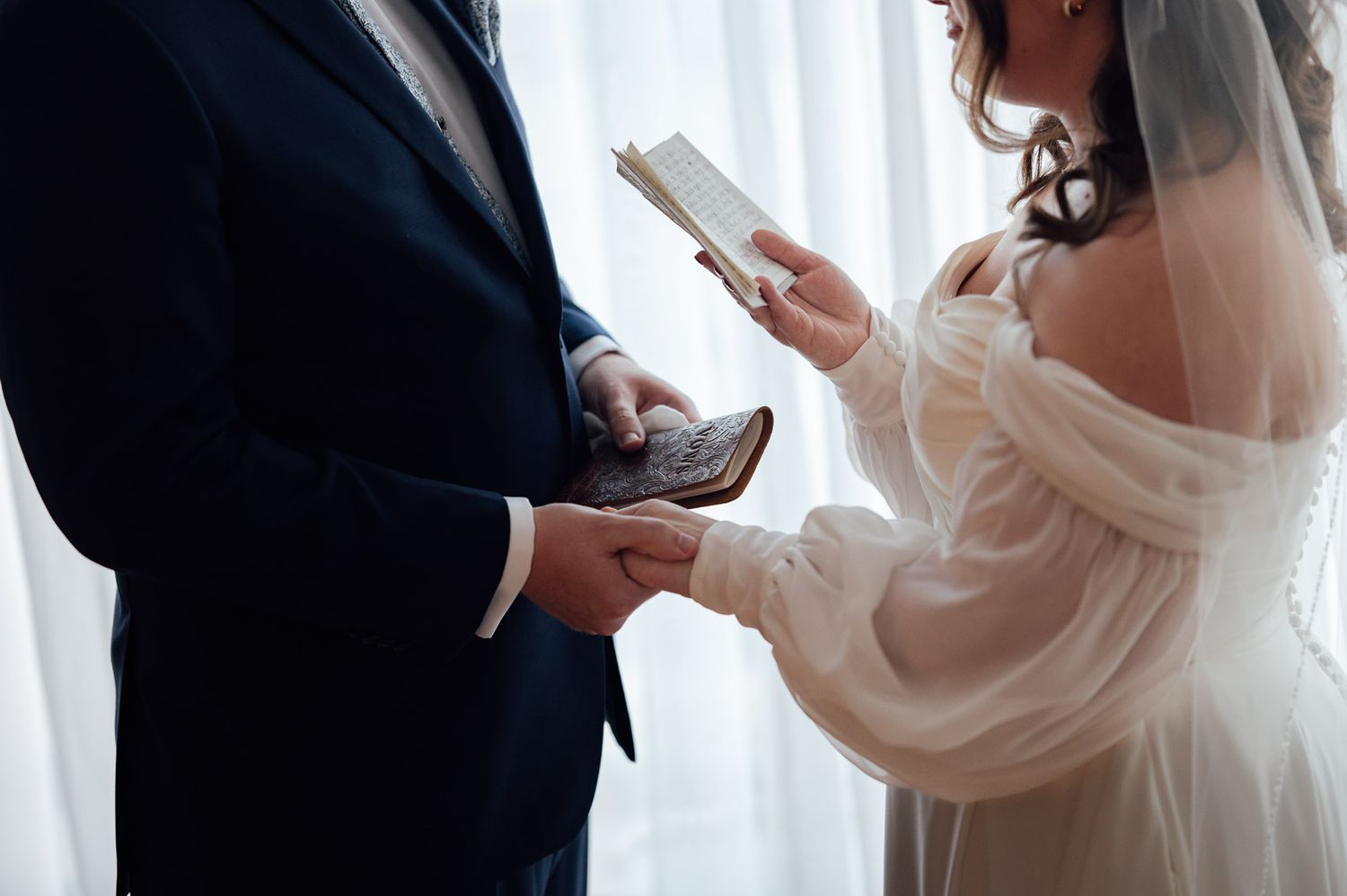 Bride and groom exchange handwritten vows holding books in soft natural window light.