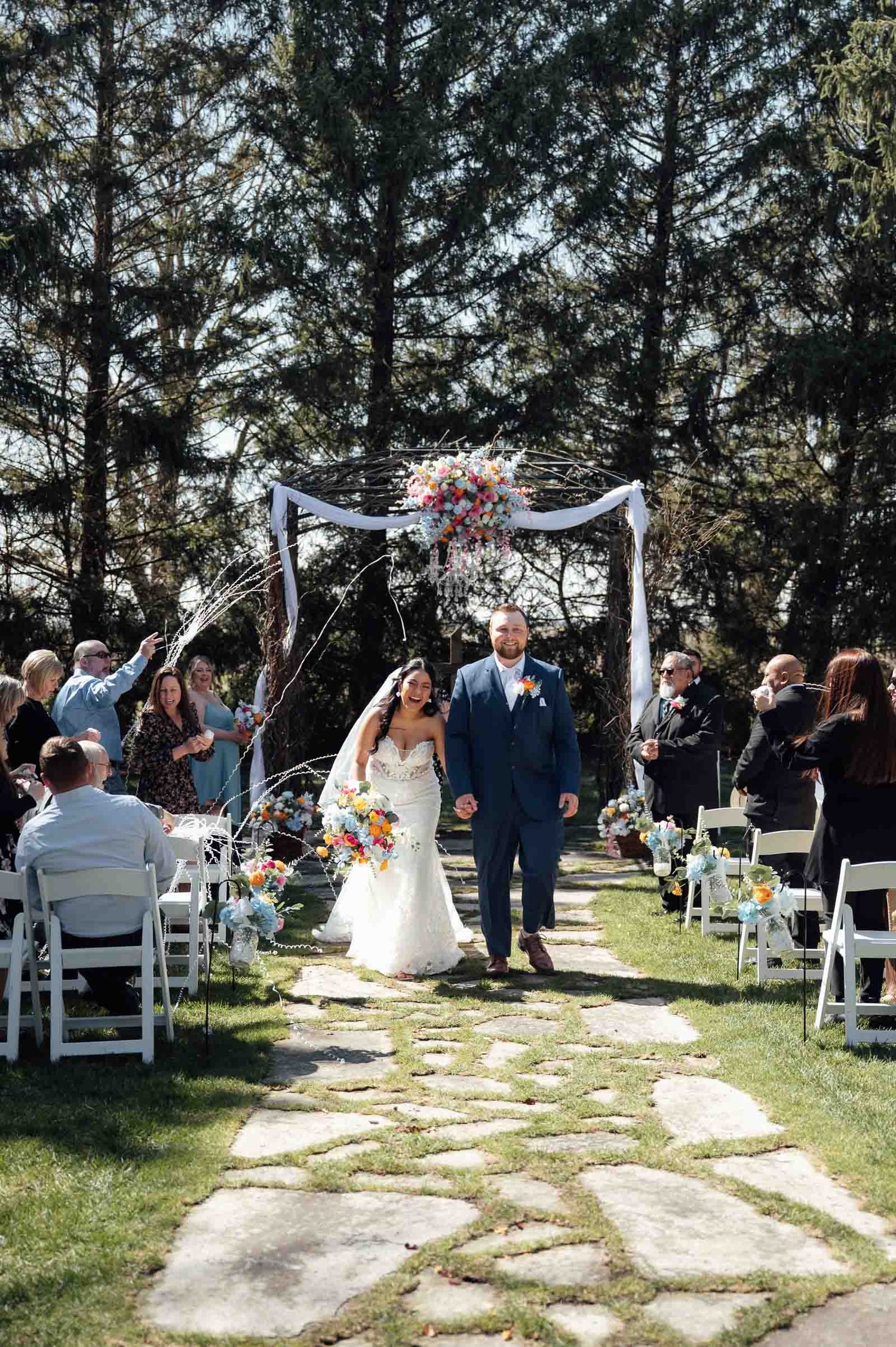 Bride and groom walk back down the aisle after outdoor wedding ceremony under a floral arch.
