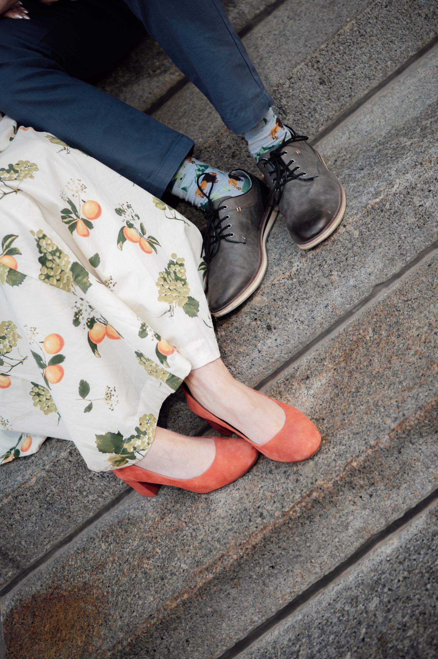 Close-up of couple's feet on stone steps, woman in coral heels and floral dress, man in patterned socks.