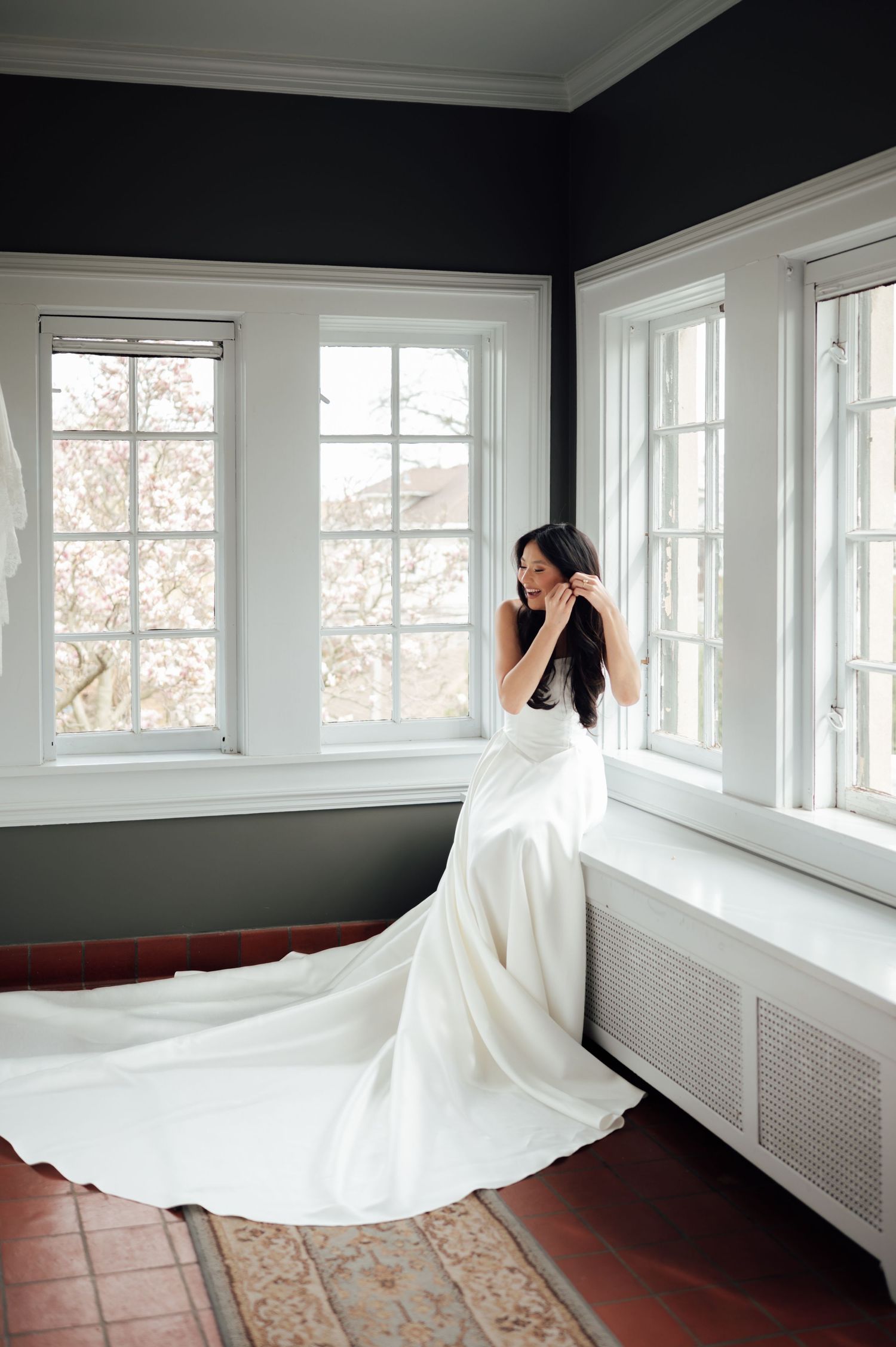 Bride in stunning white gown with long train poses by large windows in elegant room.