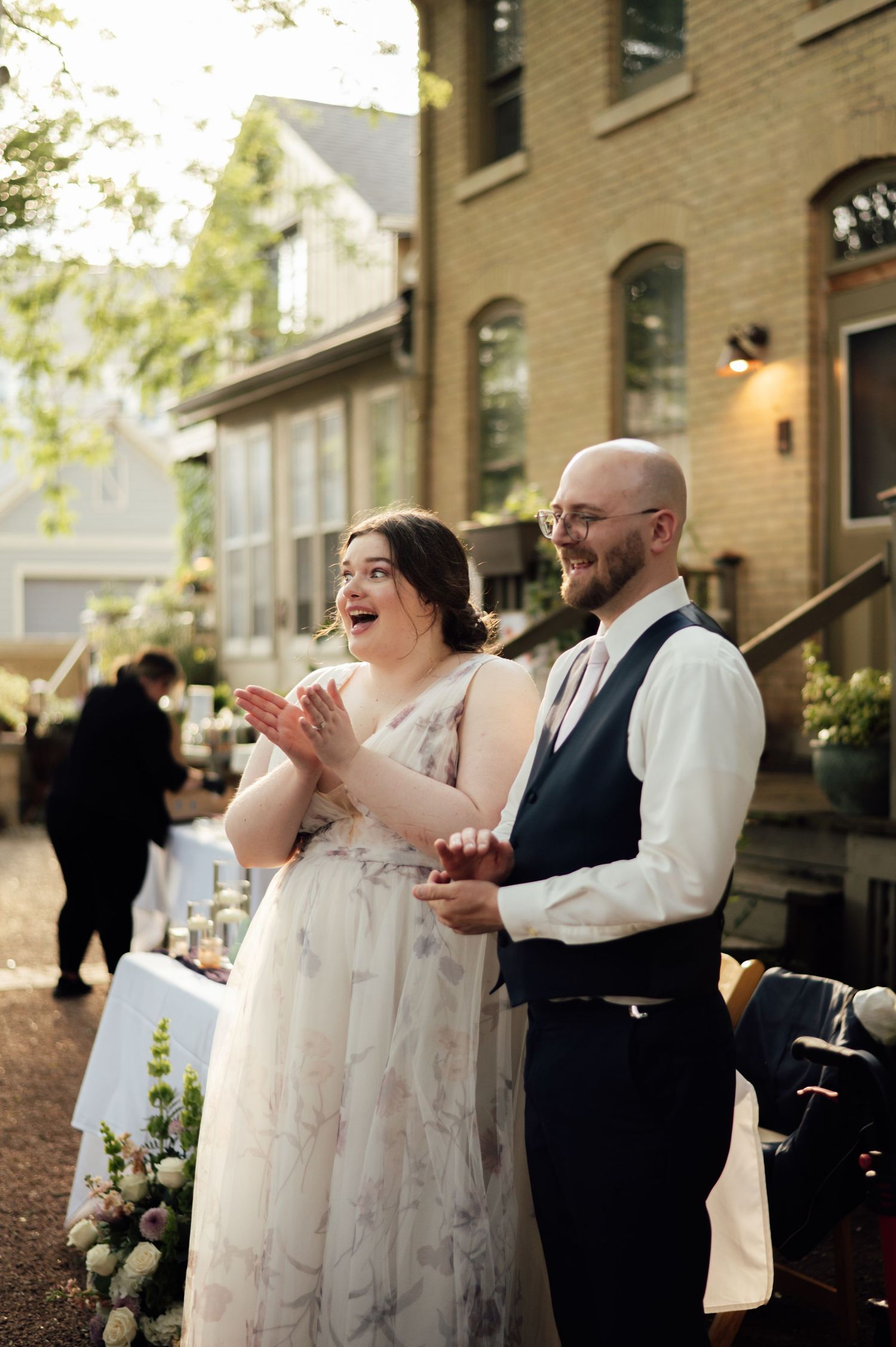 Bride and groom smiling during outdoor wedding reception beside a historic brick building.
