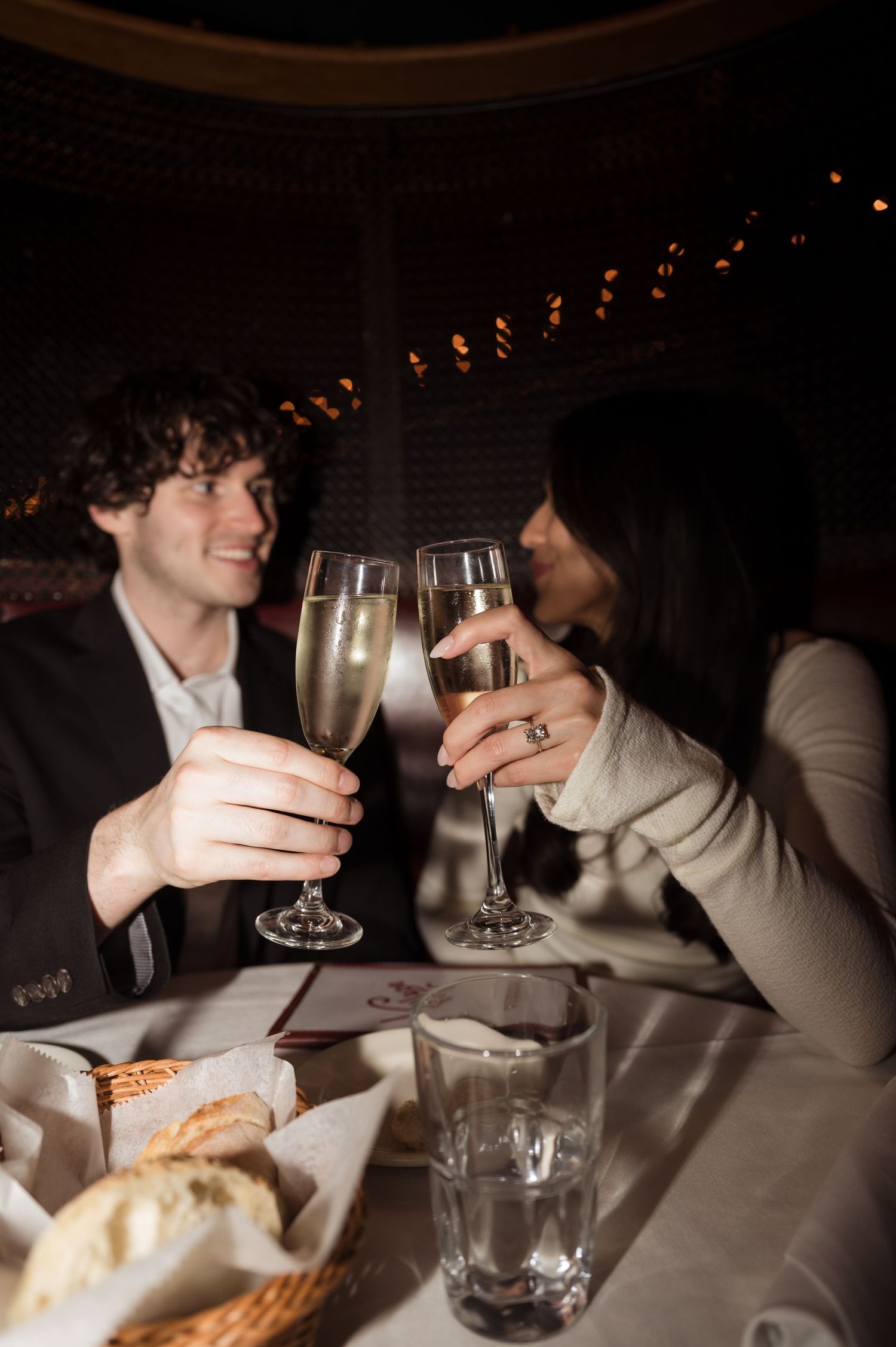Couple toasting champagne flutes at a romantic candlelit restaurant dinner date.