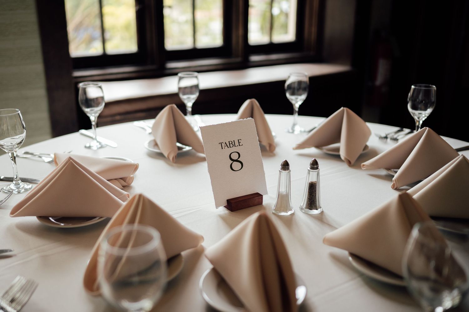 Elegant wedding reception table 8 with neatly folded beige napkins, wine glasses, and a white tablecloth.
