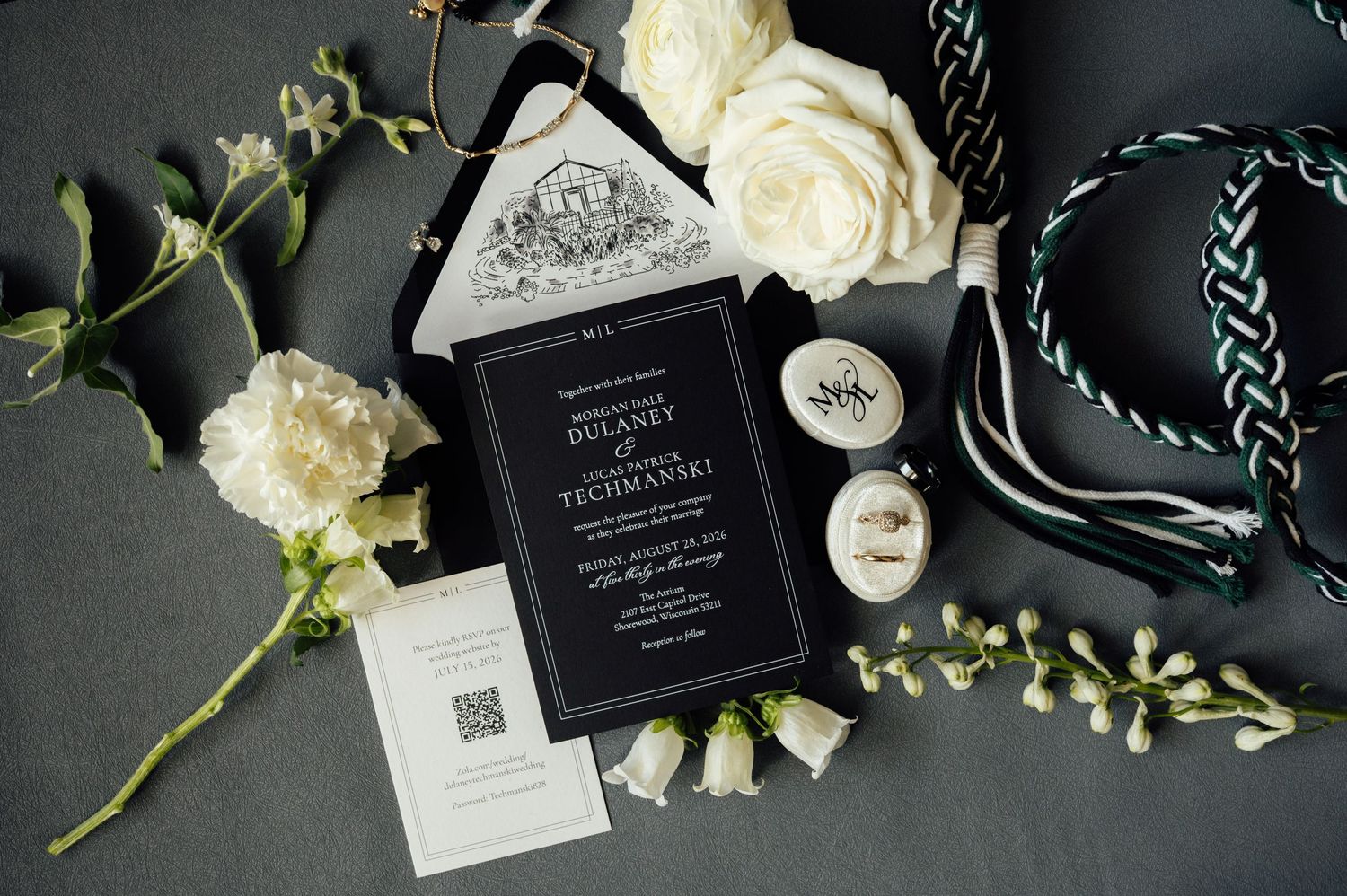 Elegant black and white wedding invitation suite with floral accents, roses, and decorative ribbon on a gray background.