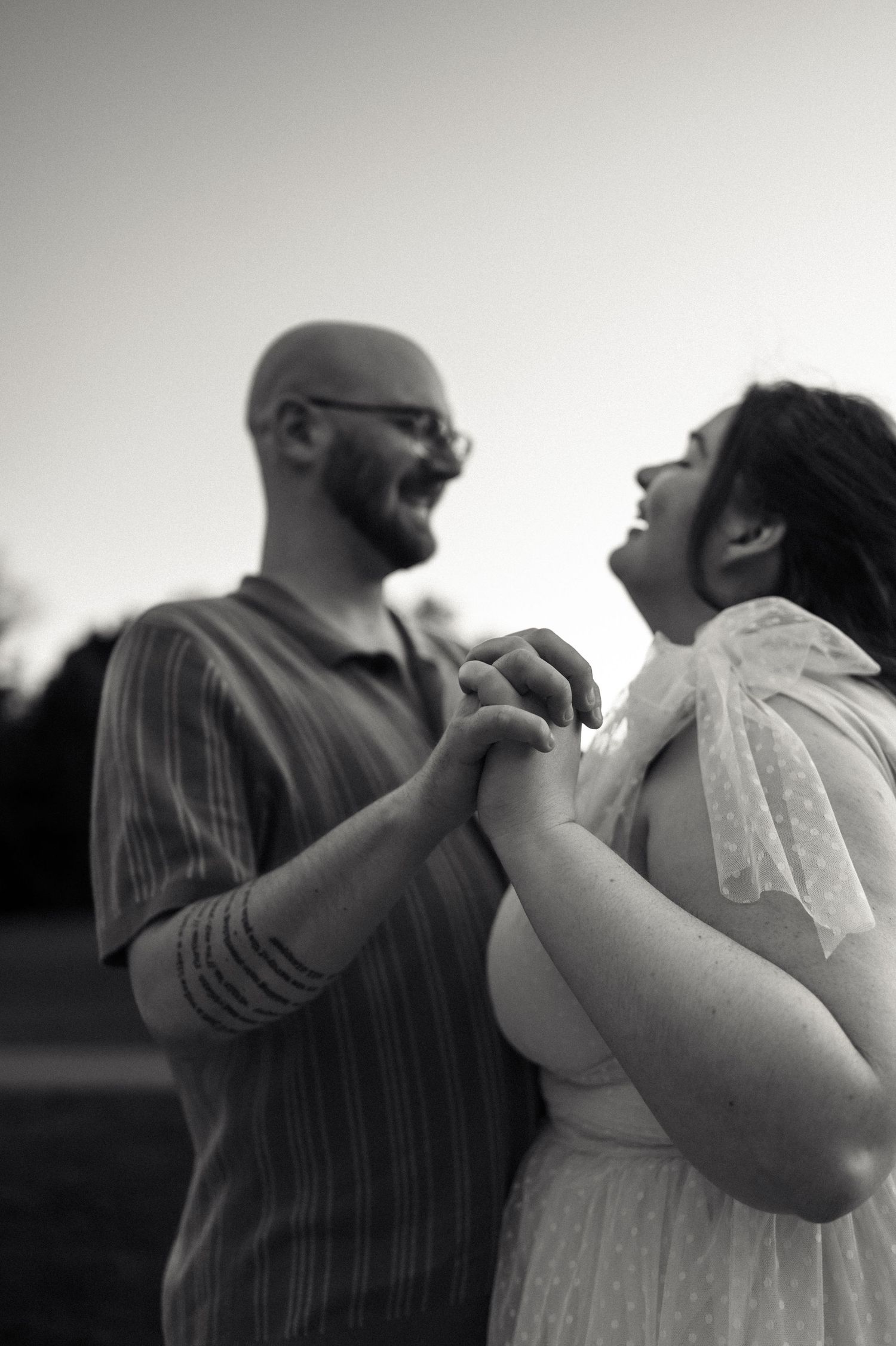 Black and white photo of laughing couple holding hands together during outdoor engagement photography session.