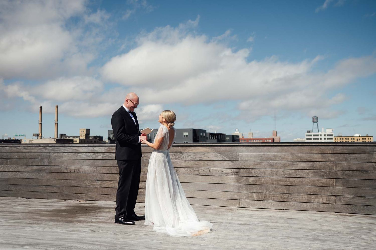 Bride and groom sharing first look moment on rooftop deck under blue cloudy sky at industrial venue.