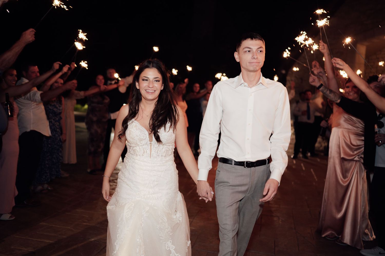 Bride and groom walk through a sparkling sparkler exit tunnel at their evening wedding reception.