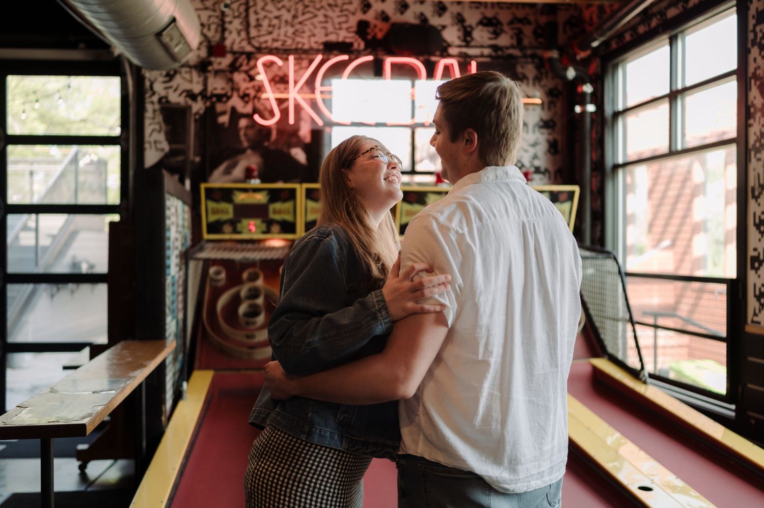 Couple laughing and dancing together inside a vibrant bar with neon signs and eclectic decor.
