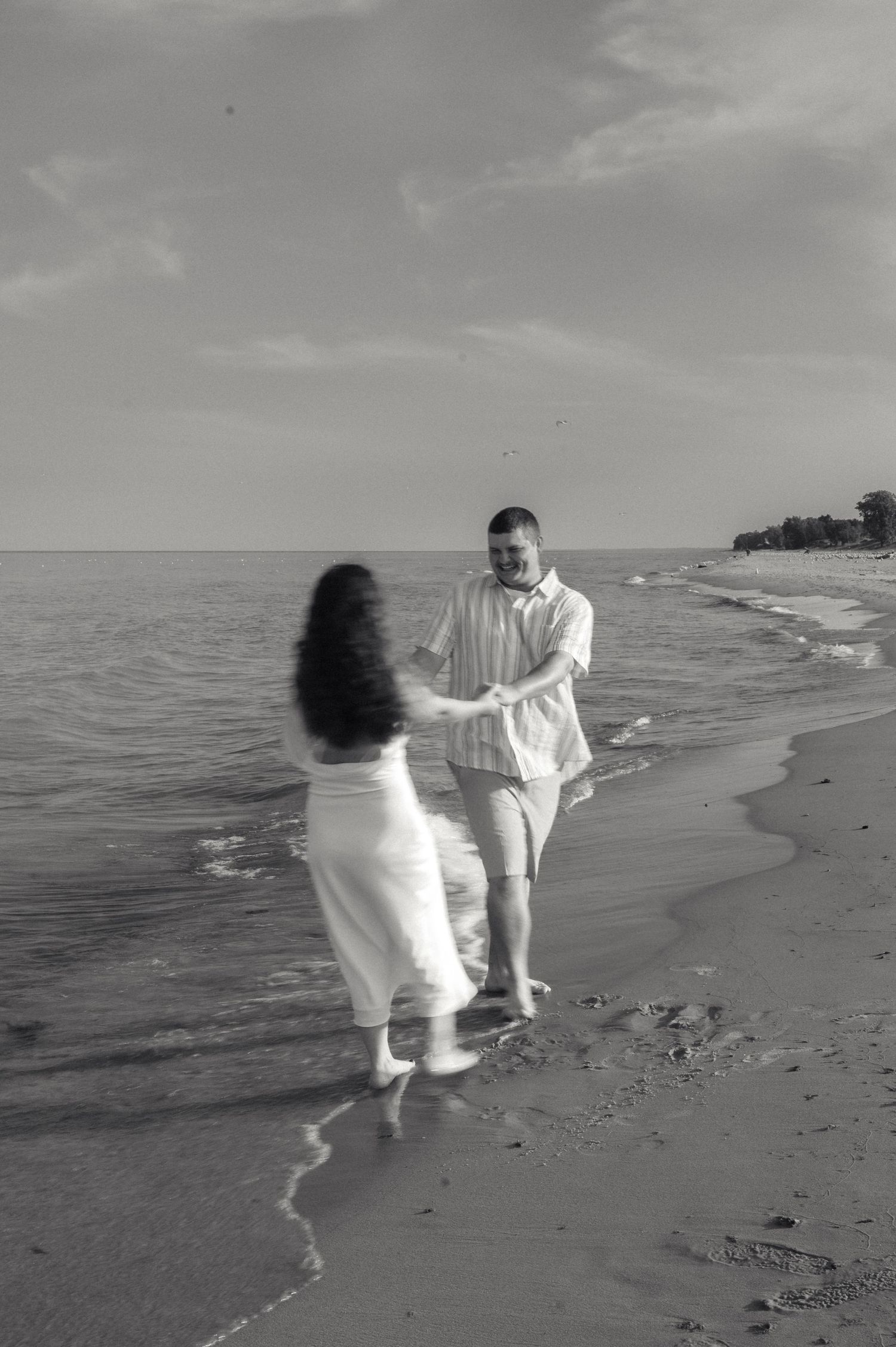 Black and white photo of couple dancing and holding hands at the edge of ocean waves.