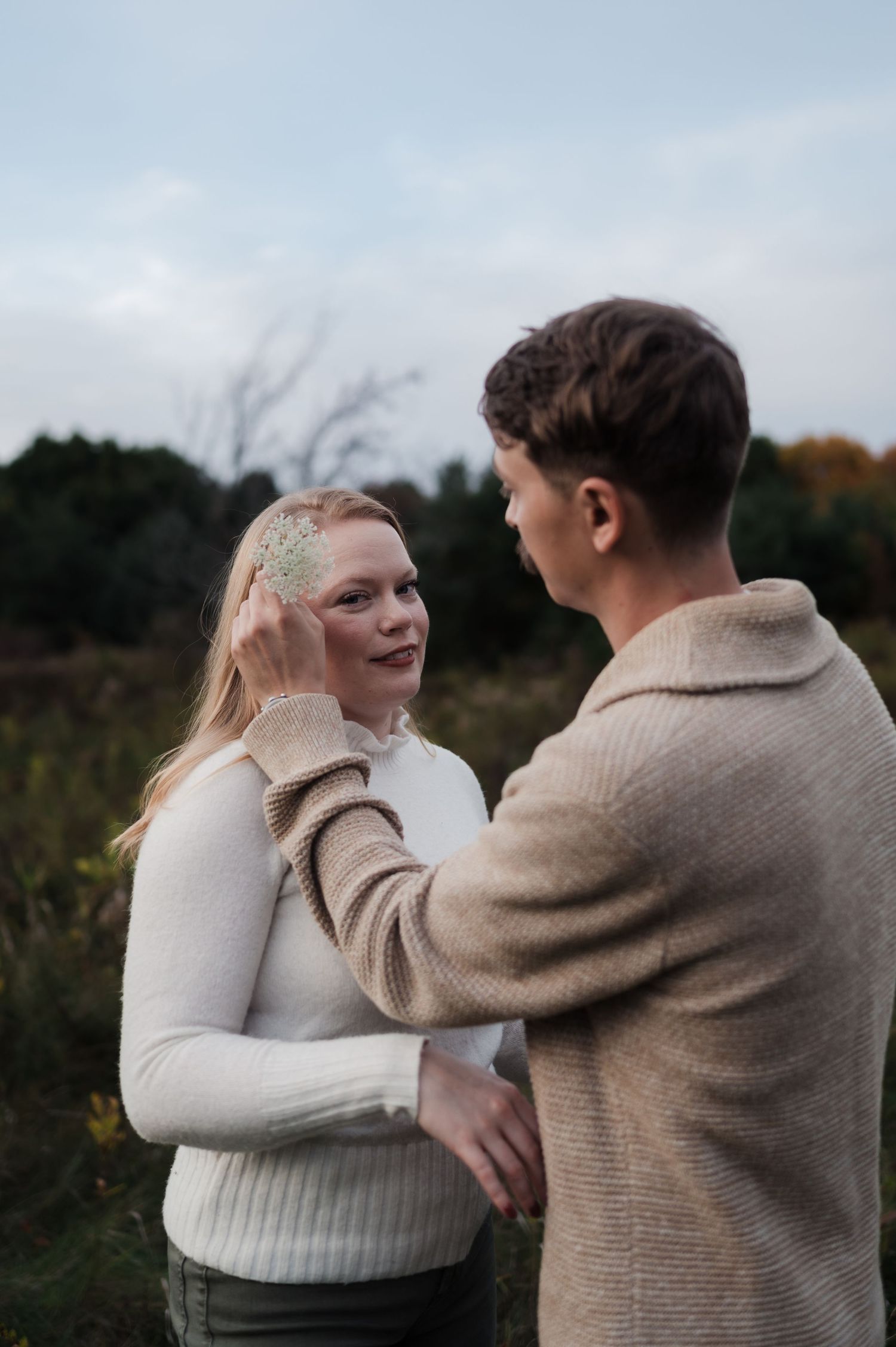 Man tenderly brushing hair from smiling blonde woman's face during outdoor engagement session in a field.