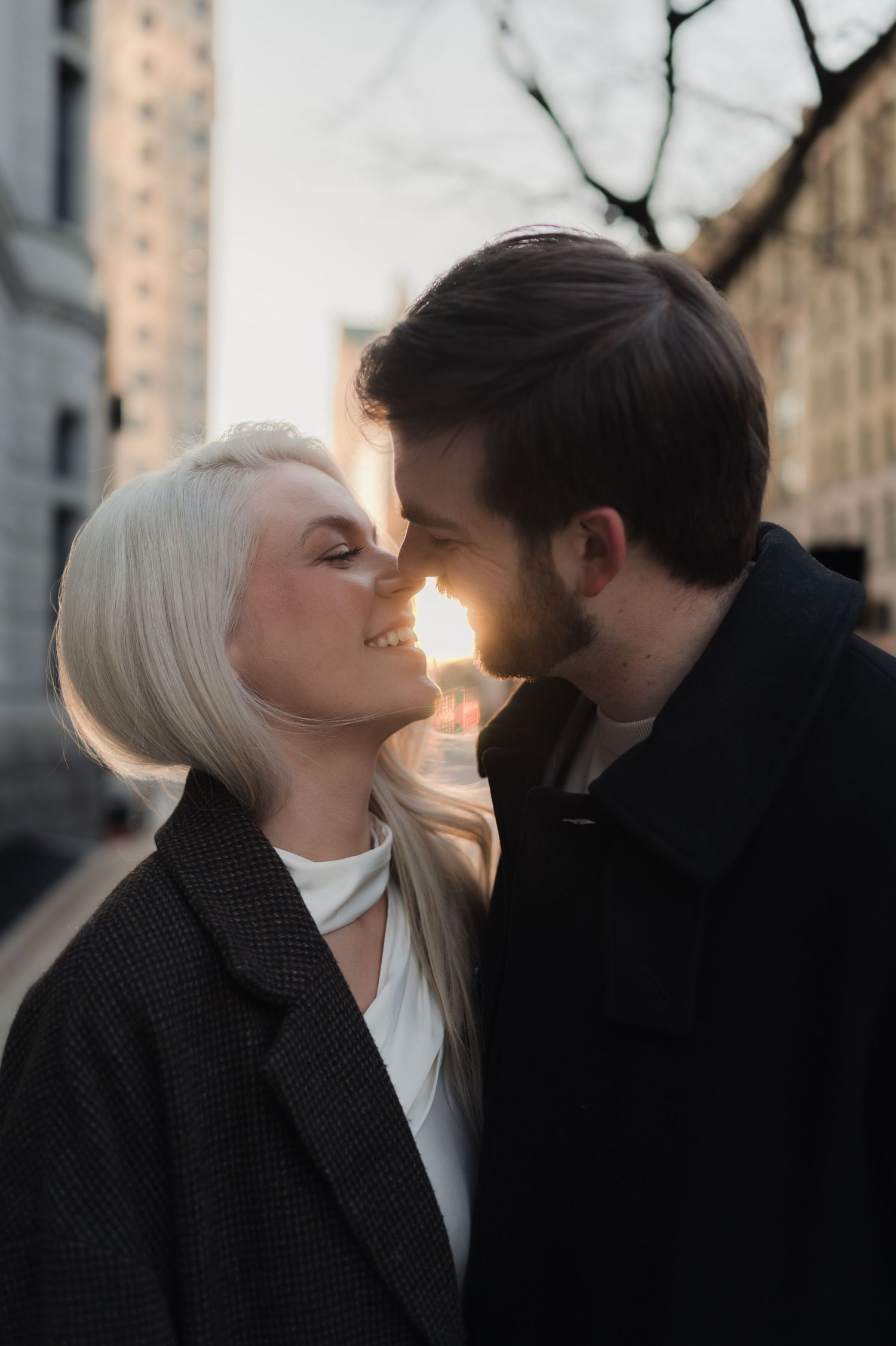 Romantic couple leaning in for a kiss with golden sunlight glowing between them on a city street.