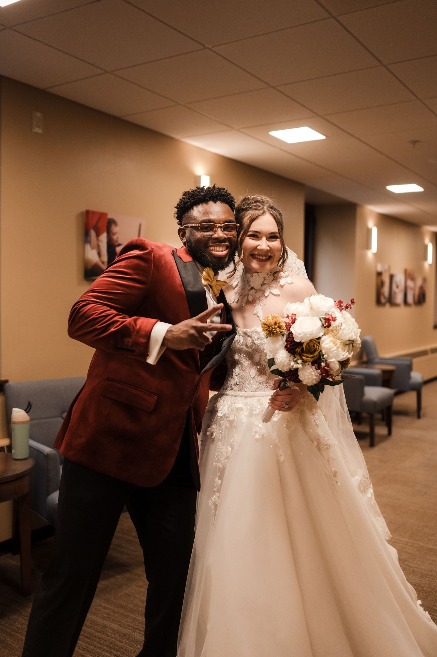 A wedding couple shares a sweet moment in a church hallway as they lean in close together in burgundy and white attire.