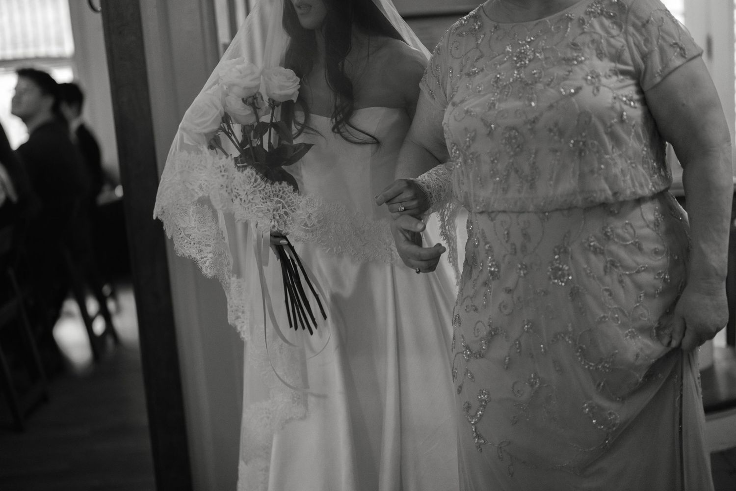 Black and white photo of bride holding bouquet standing beside mother before ceremony.