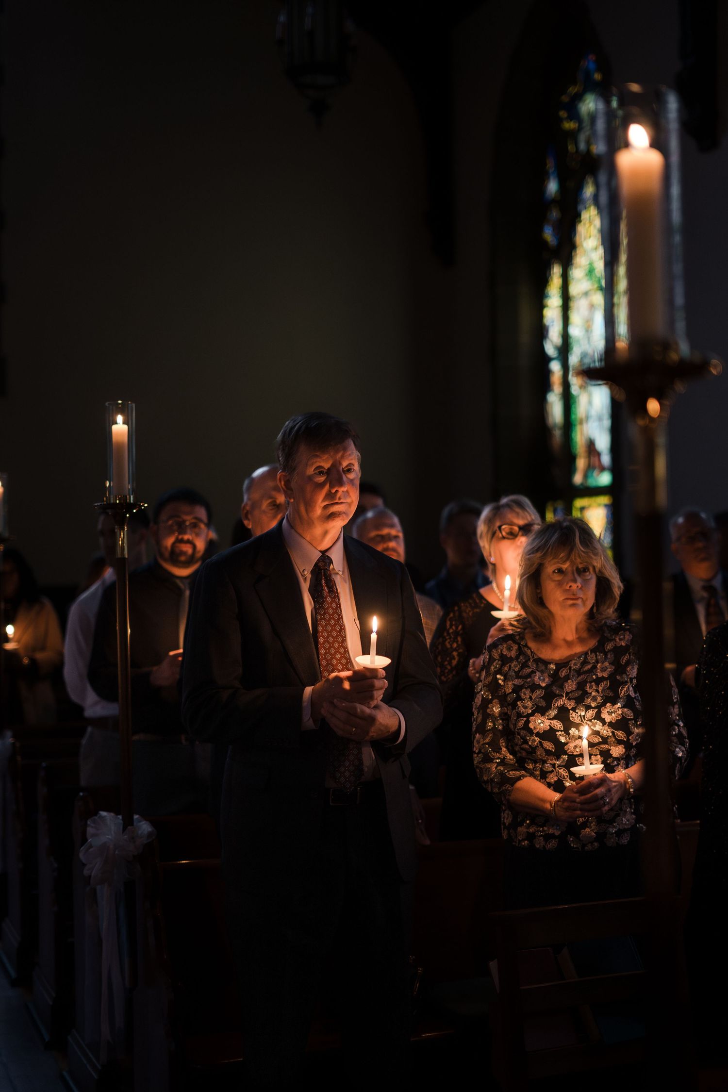 A candlelit church service shows silhouettes of people holding candles in a darkened sanctuary.
