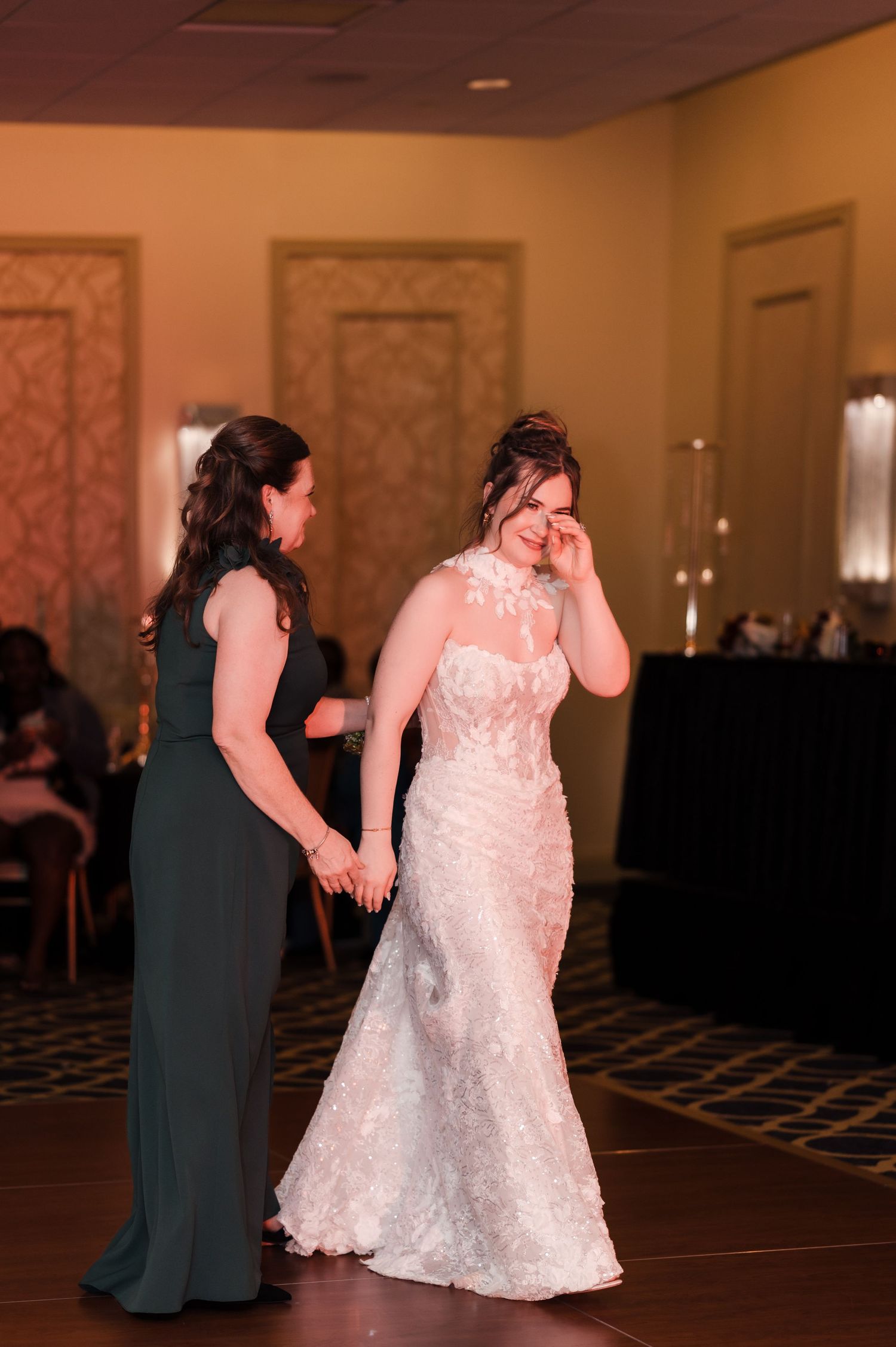 Wedding reception dance sequence showing a bride in white lace gown dancing with a guest in a dark formal dress.