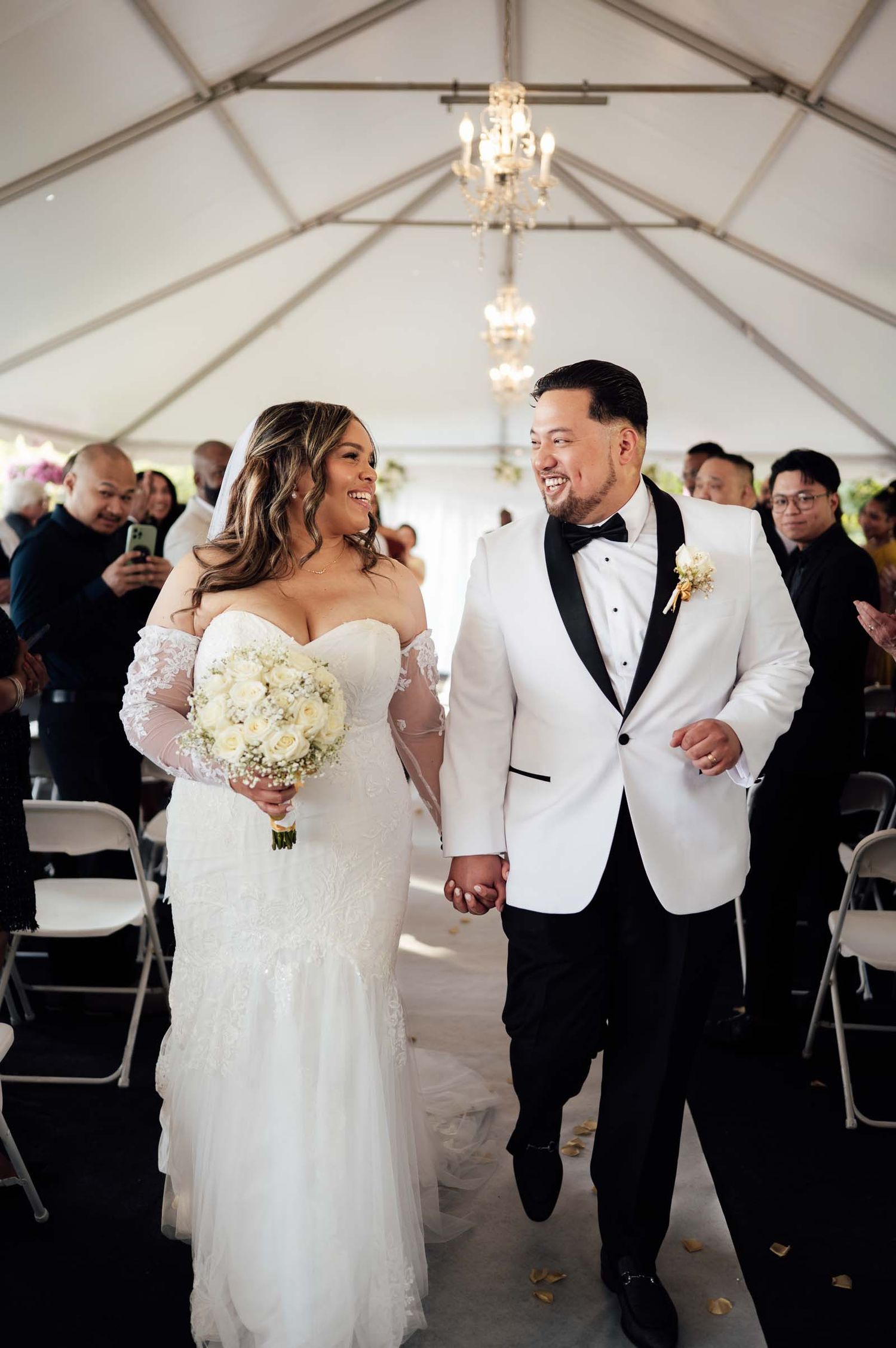 Bride and groom share a loving glance while walking down the aisle at their elegant tented wedding.