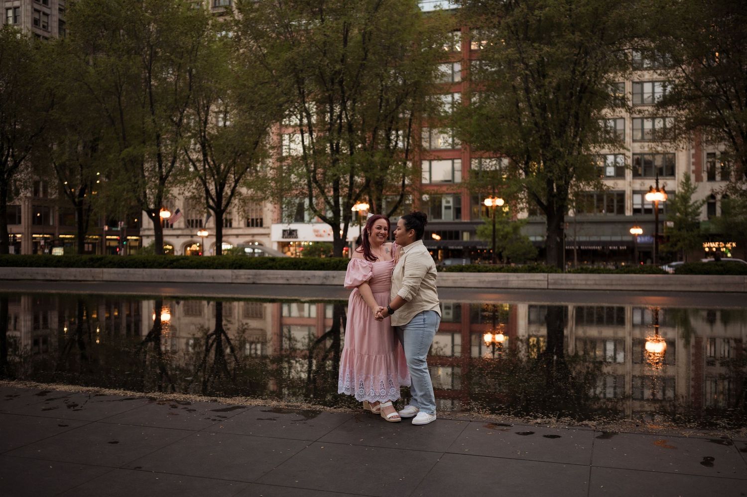Couple embracing romantically by a reflective pond in an urban park at dusk.