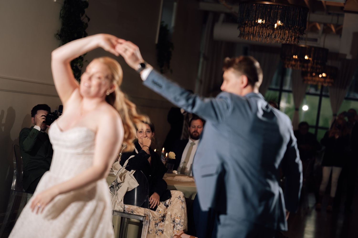 Bride and groom share first dance at wedding reception, with guests watching in elegant venue.