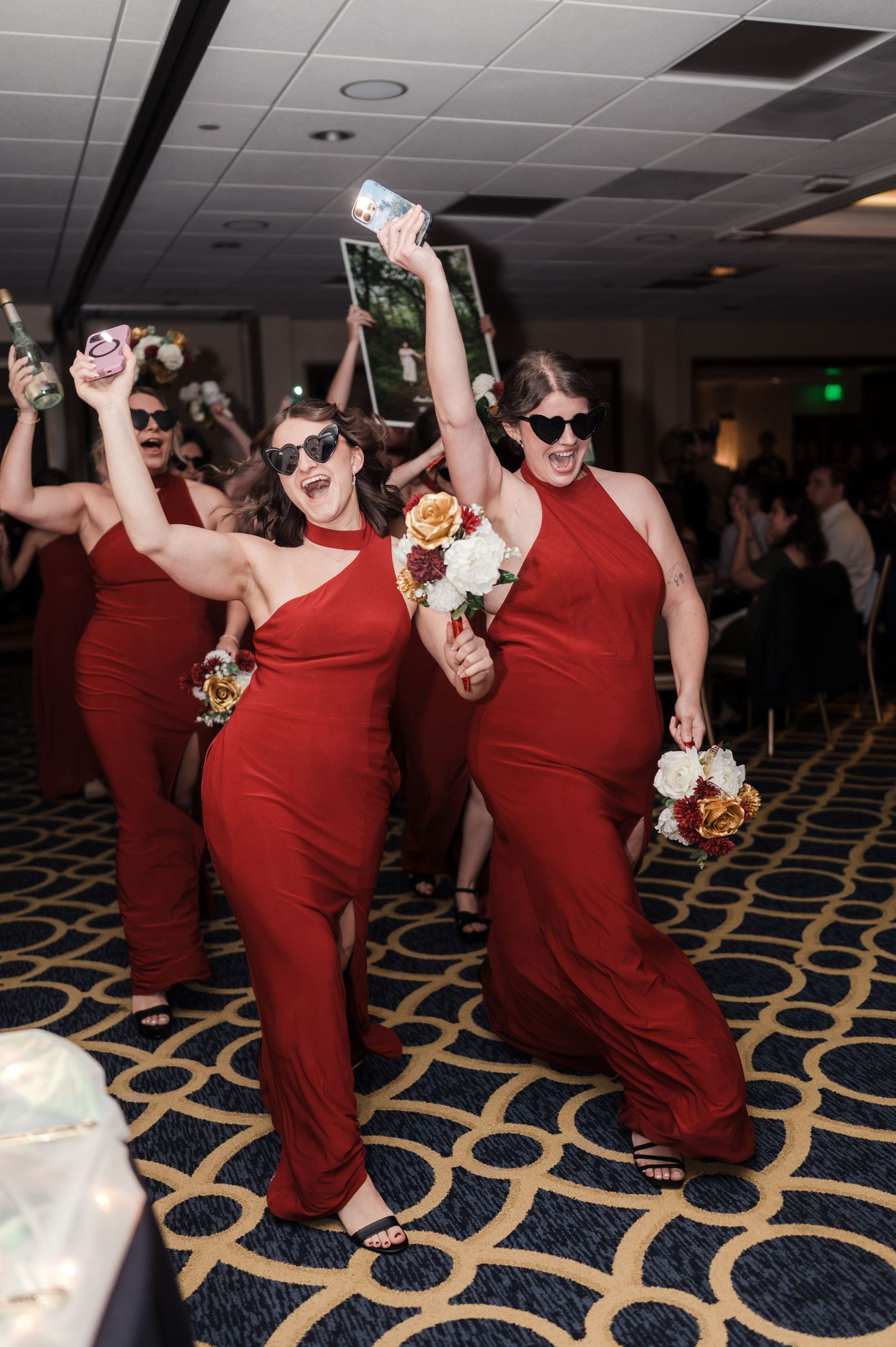 Group of people in matching red outfits dancing and celebrating on a patterned carpet at an indoor event.