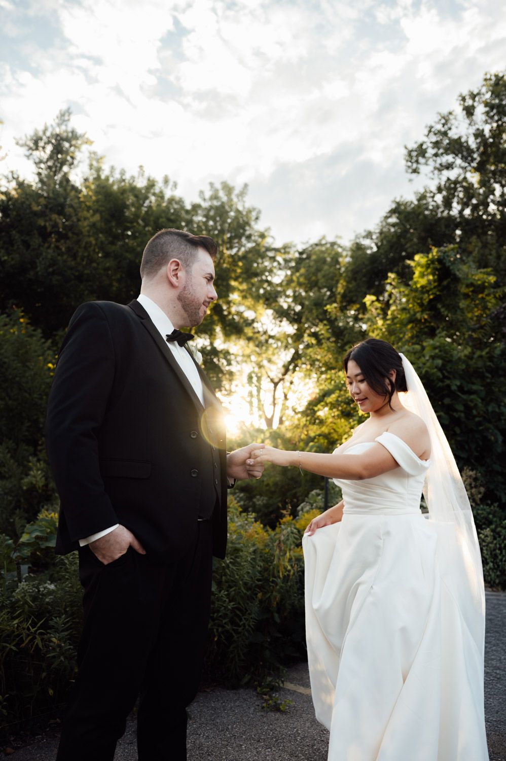 Bride and groom holding hands in garden at golden hour sunset during wedding portraits.