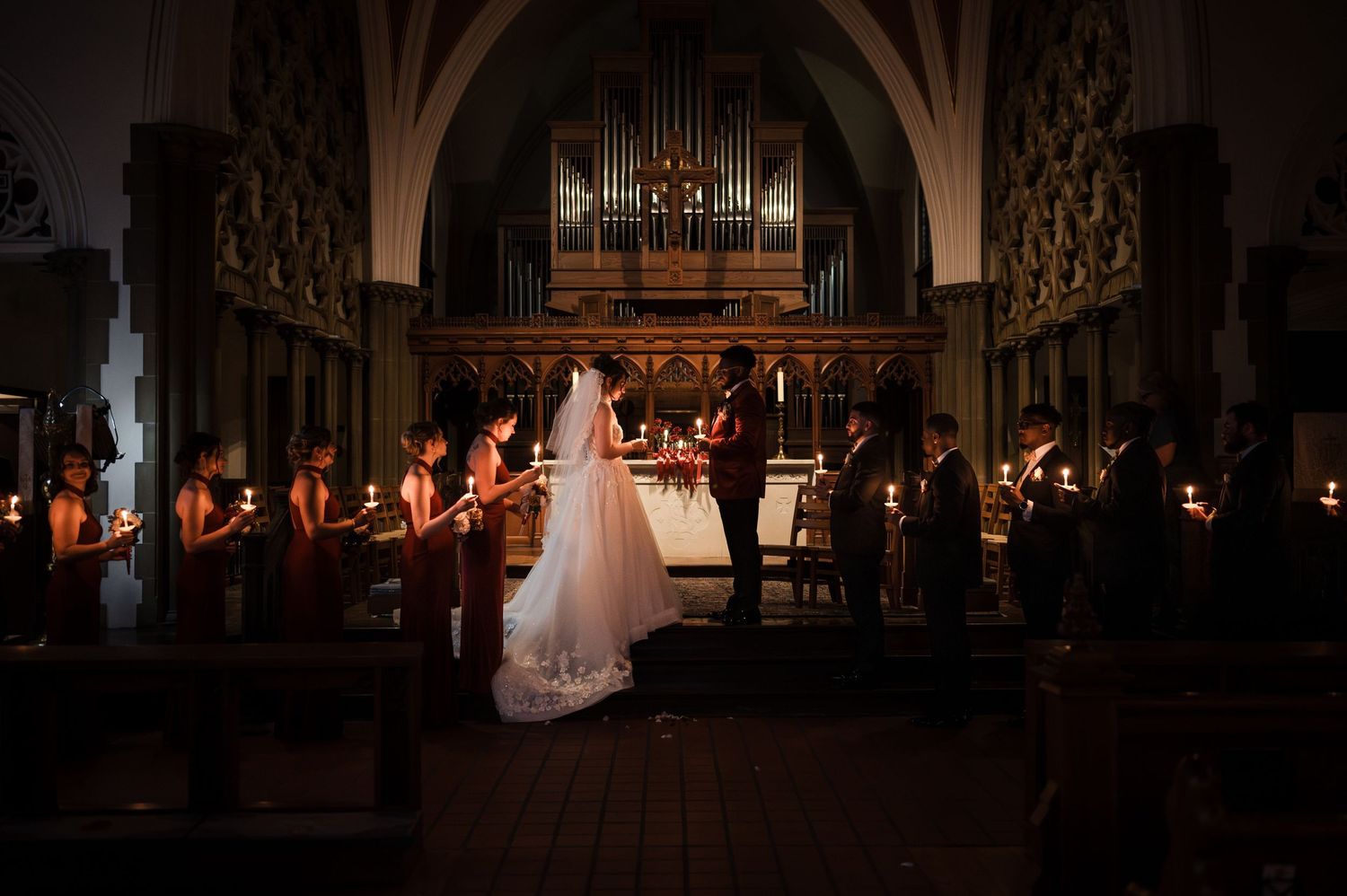Candlelit church wedding ceremony with bride, groom, and wedding party gathered at the altar before a pipe organ.