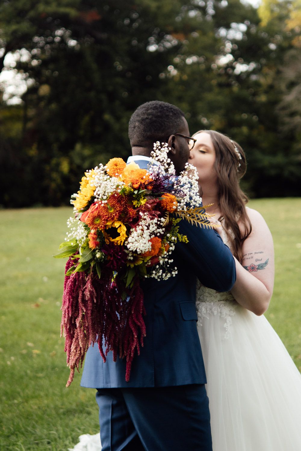 Bride and groom share first kiss surrounded by a vibrant colorful autumn wedding bouquet outdoors.