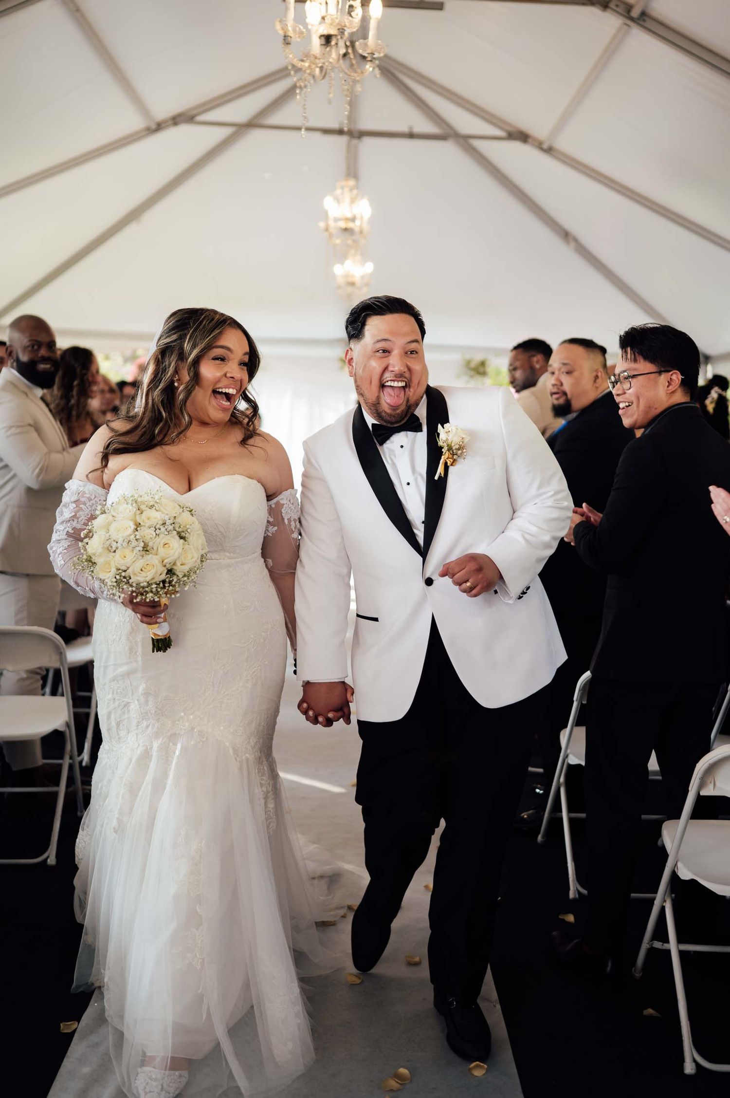 Bride and groom laugh joyfully while walking back down the aisle at their tented wedding ceremony.