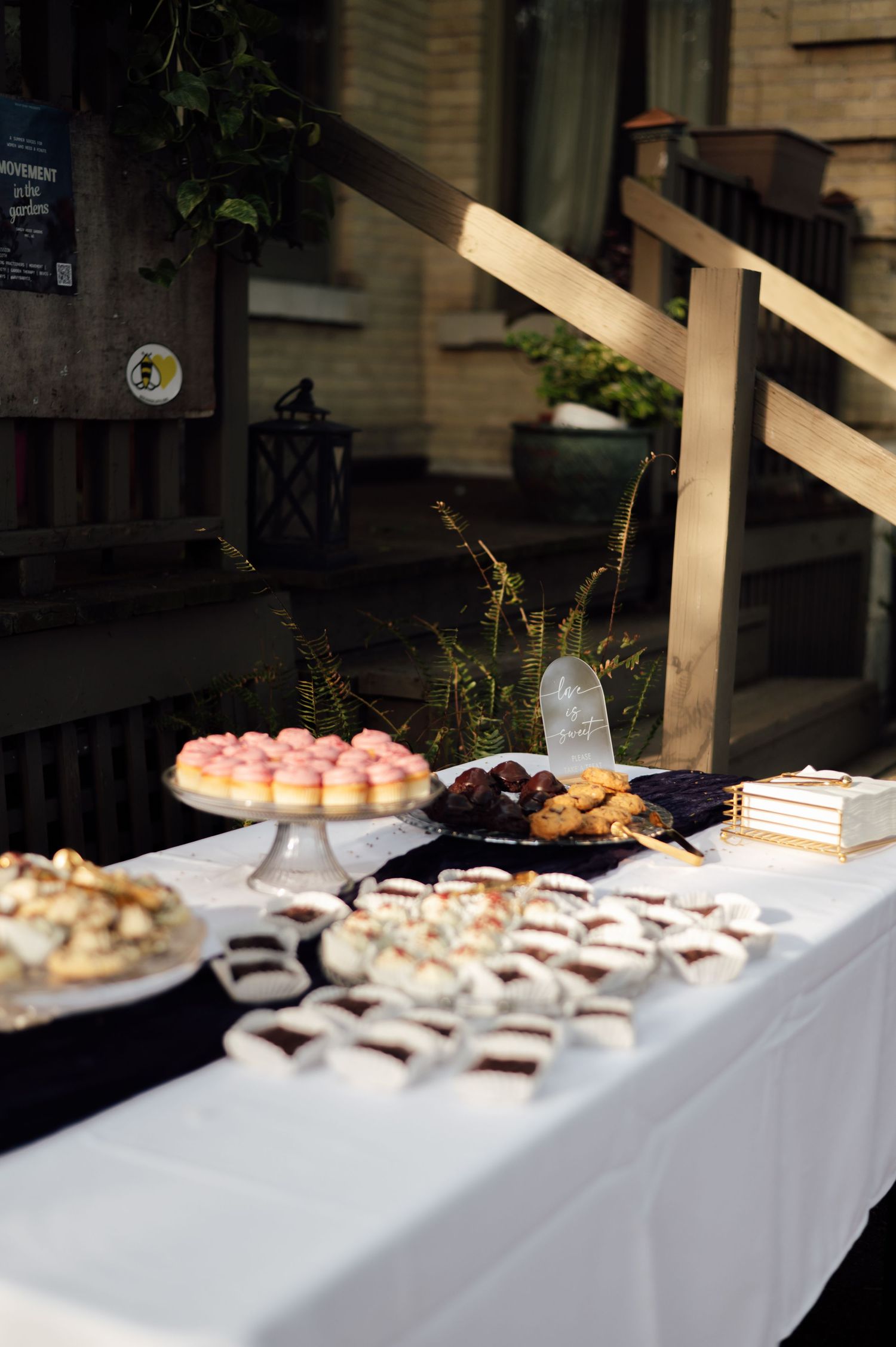 Outdoor dessert table with white tablecloth featuring donuts, cookies, and chocolate treats at a garden party.