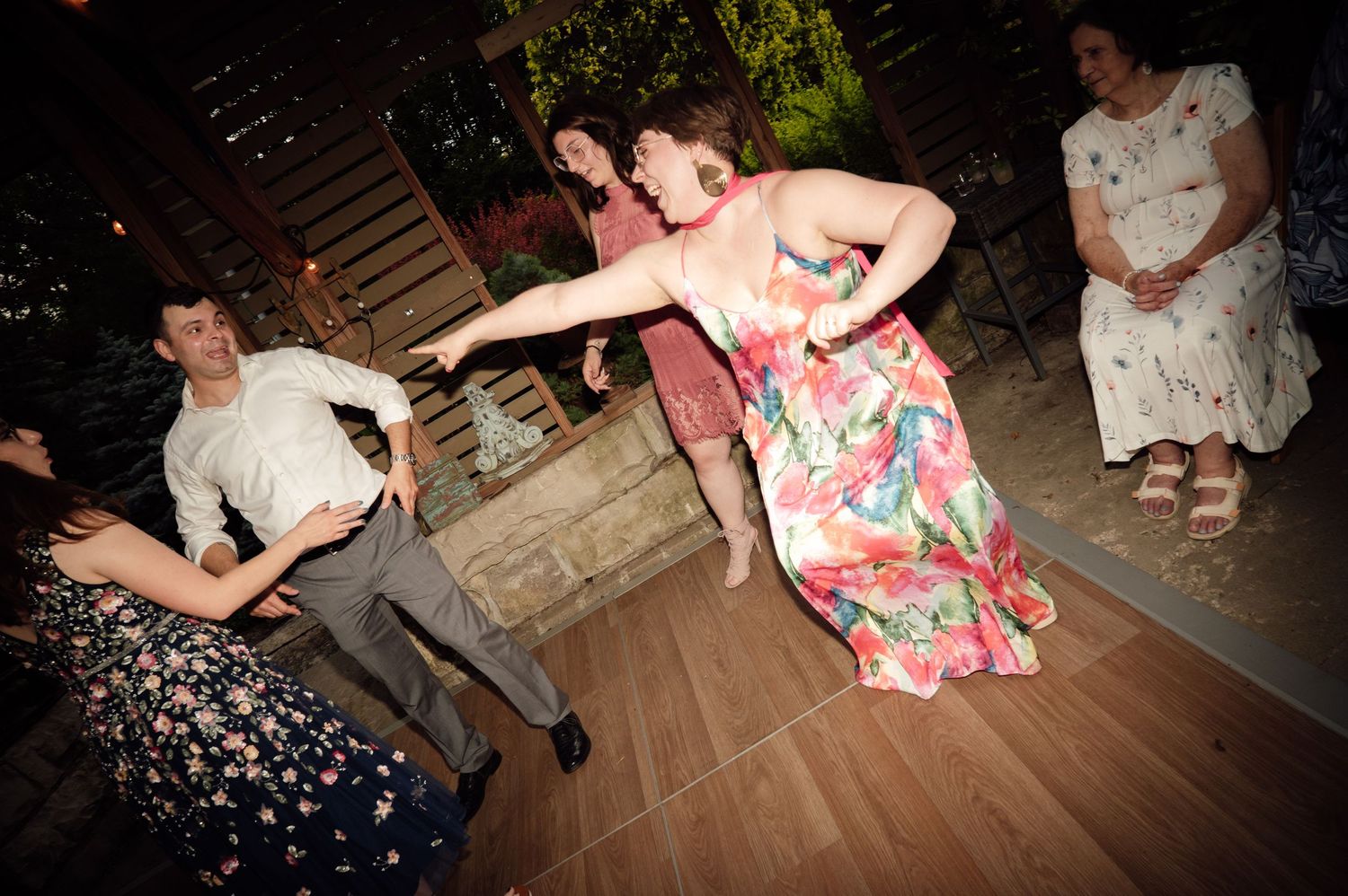 Guests dancing energetically at a wedding reception, woman in floral dress twirling on the dance floor.