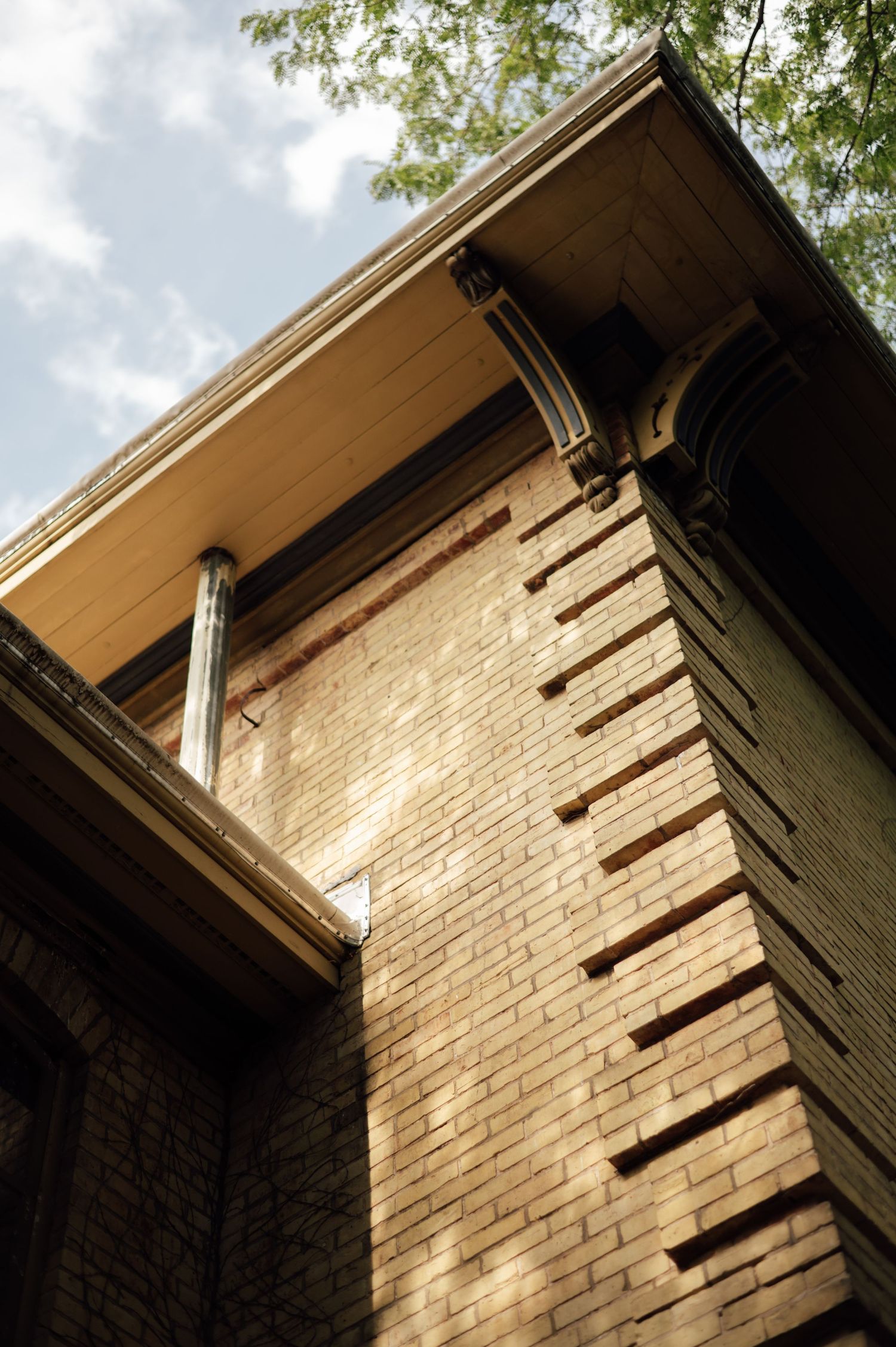 Low-angle view of a historic brick building corner with decorative column and wide overhanging eave against a cloudy sky.