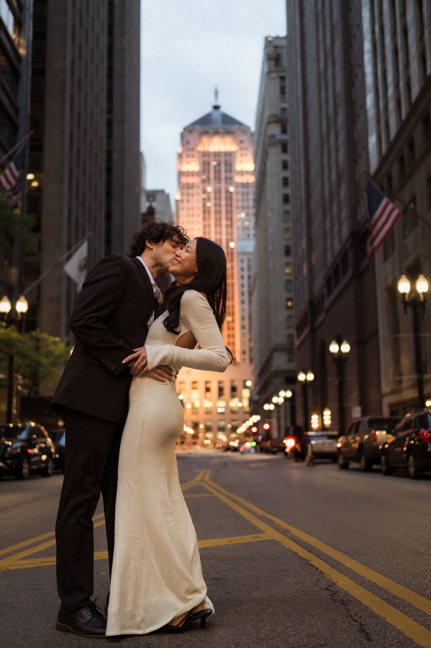 Bride and groom kissing in the middle of a Chicago street with illuminated skyscrapers in the background.