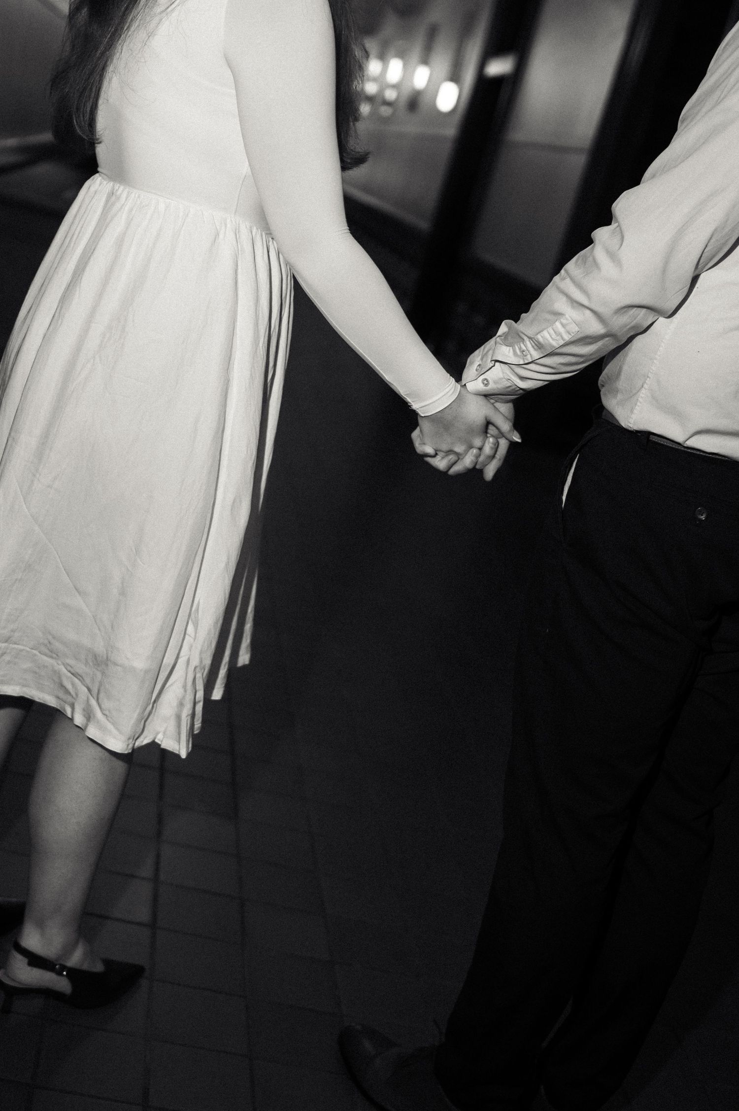Black and white photo of a couple holding hands, woman in white dress and man in dark pants.