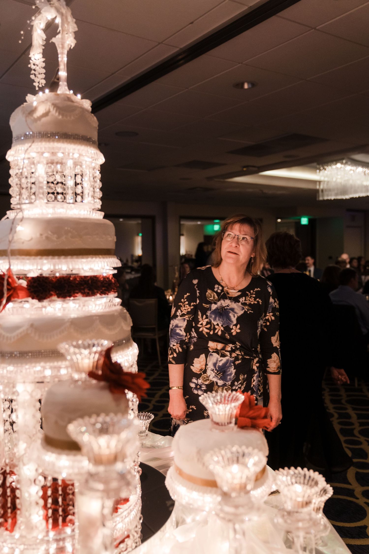 Illuminated white wedding cakes displayed on crystal stands with cascading lights at an elegant reception.