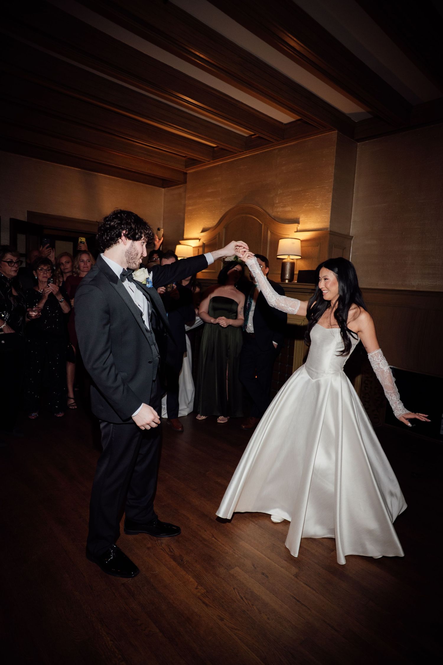 Bride in white ballgown and groom in tuxedo share energetic first dance at wedding reception.