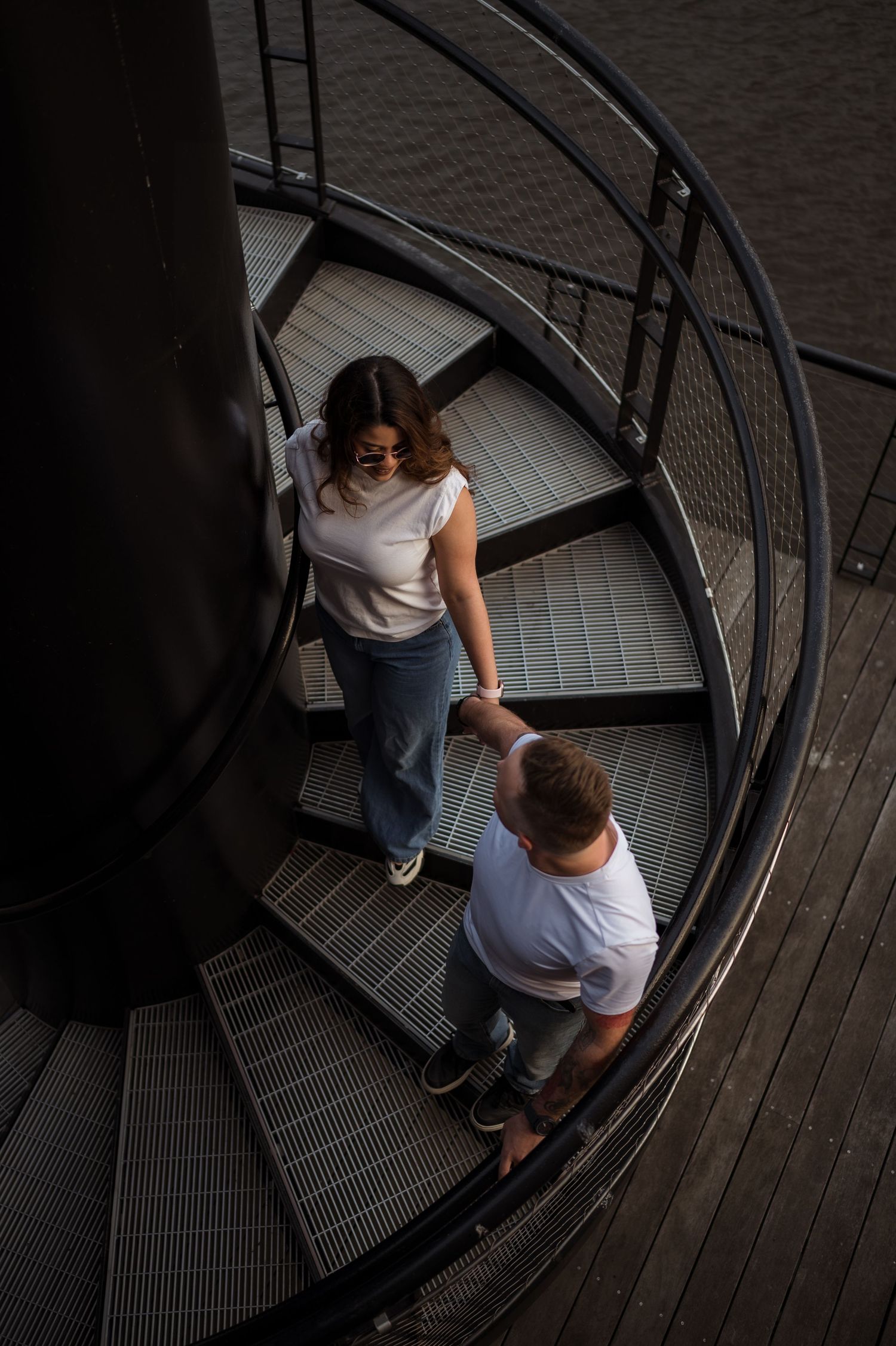 Aerial view of a couple holding hands on a modern spiral metal staircase.