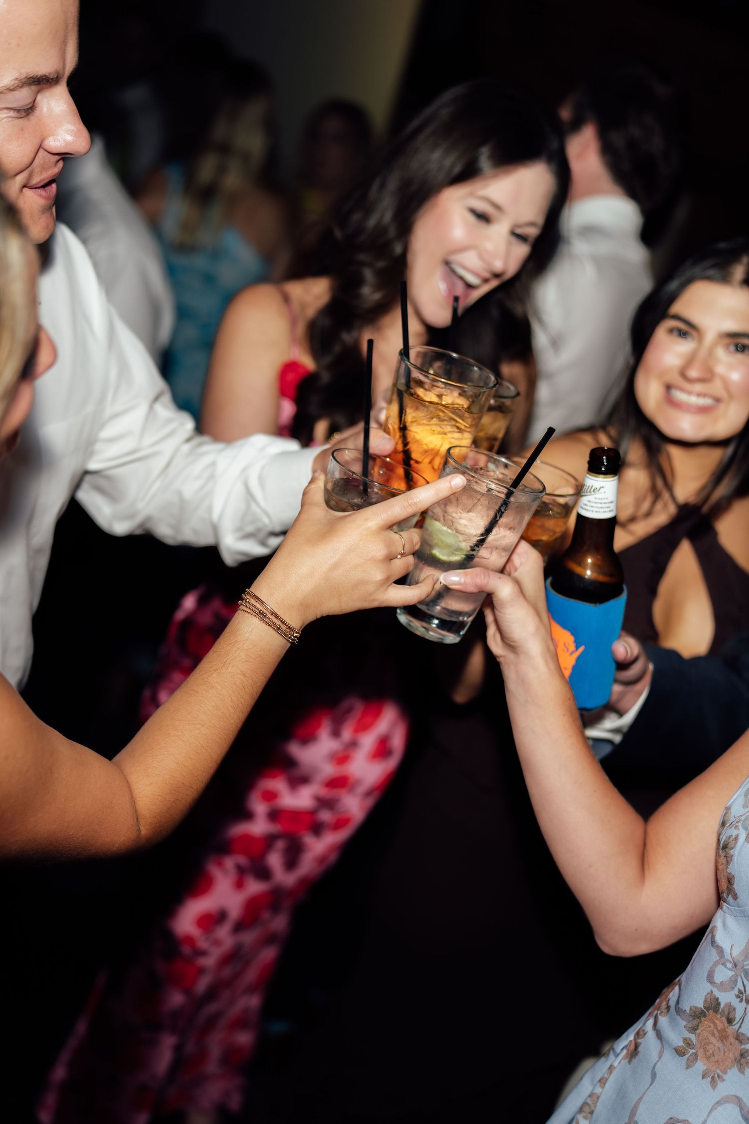 Friends toasting cocktails and beer at a lively party, laughing and celebrating together.