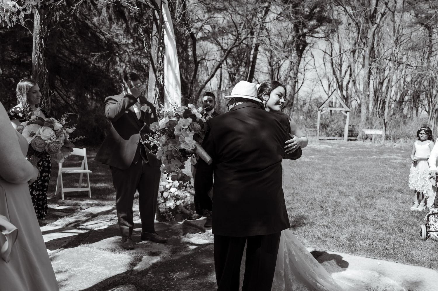 A black and white photograph of several people gathered outdoors at a formal event in a garden setting.