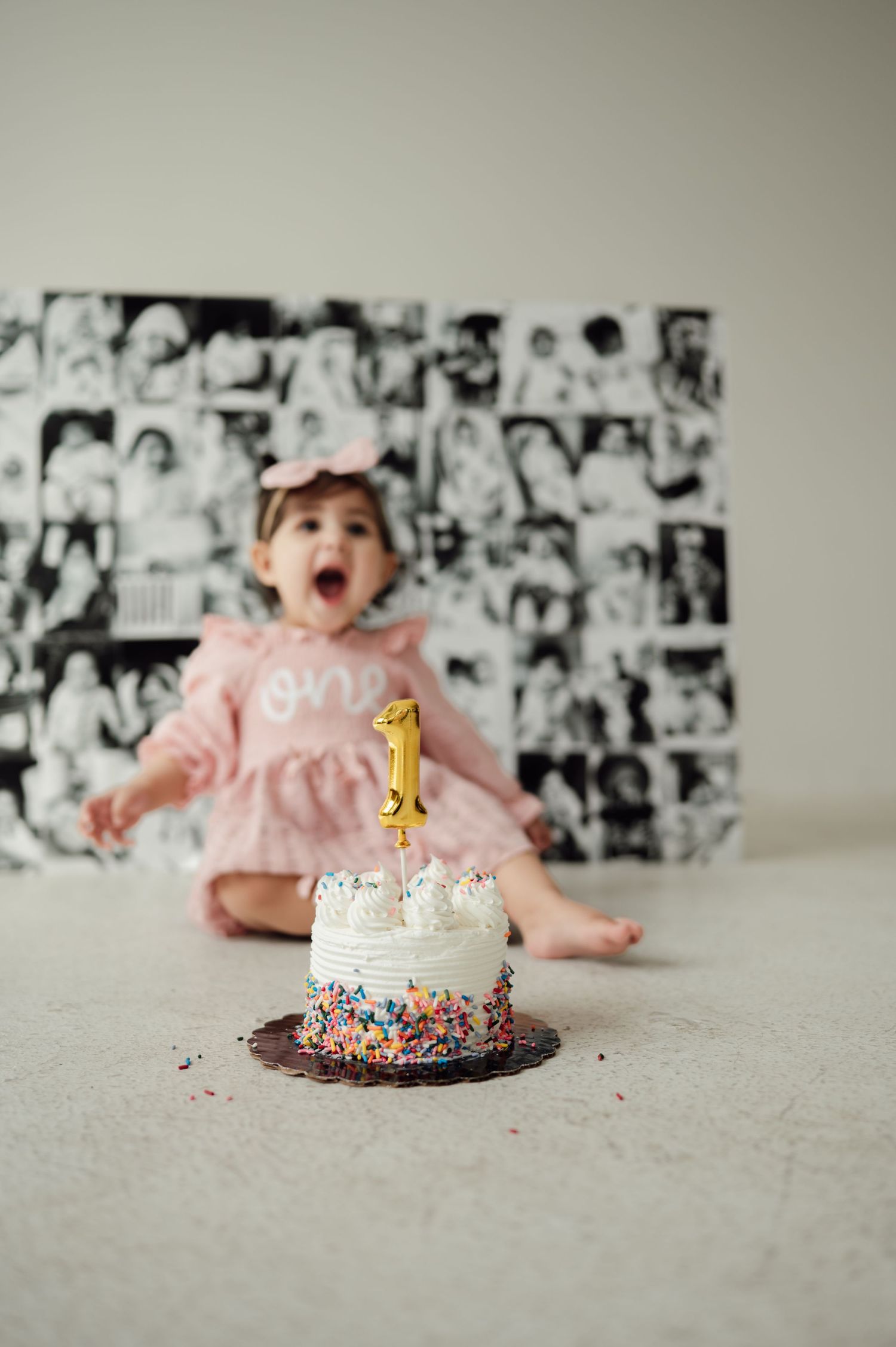 Baby girl in pink dress excited at first birthday cake smash with number one candle.