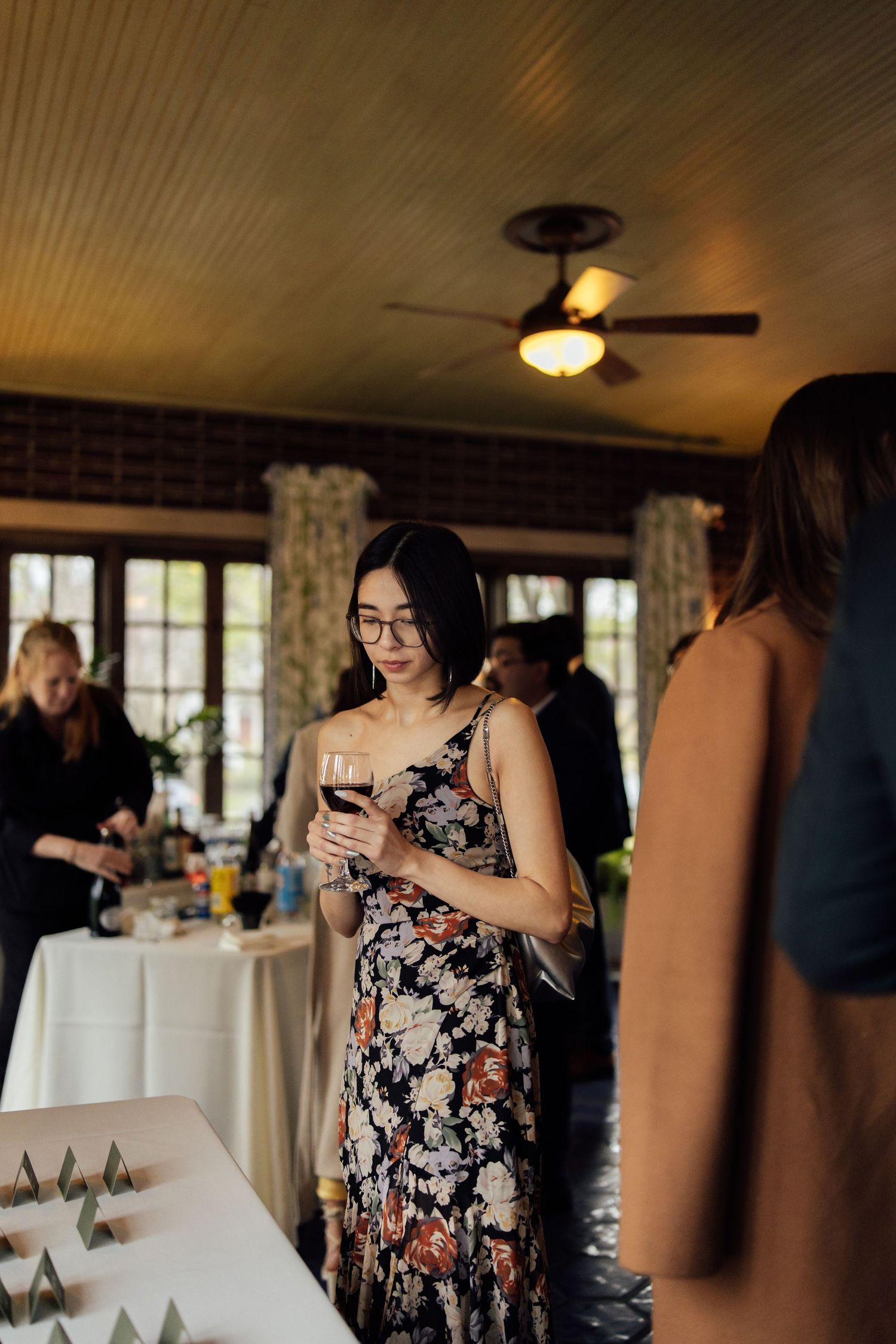 Woman in floral dress holding red wine glass at an elegant indoor social gathering event.