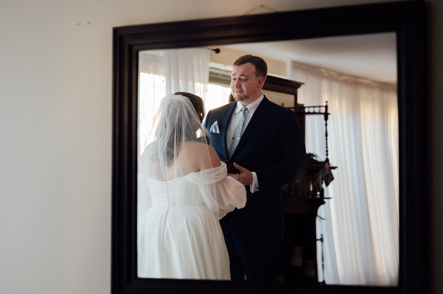 Bride and groom share a tender first look moment reflected in an ornate mirror before the wedding.
