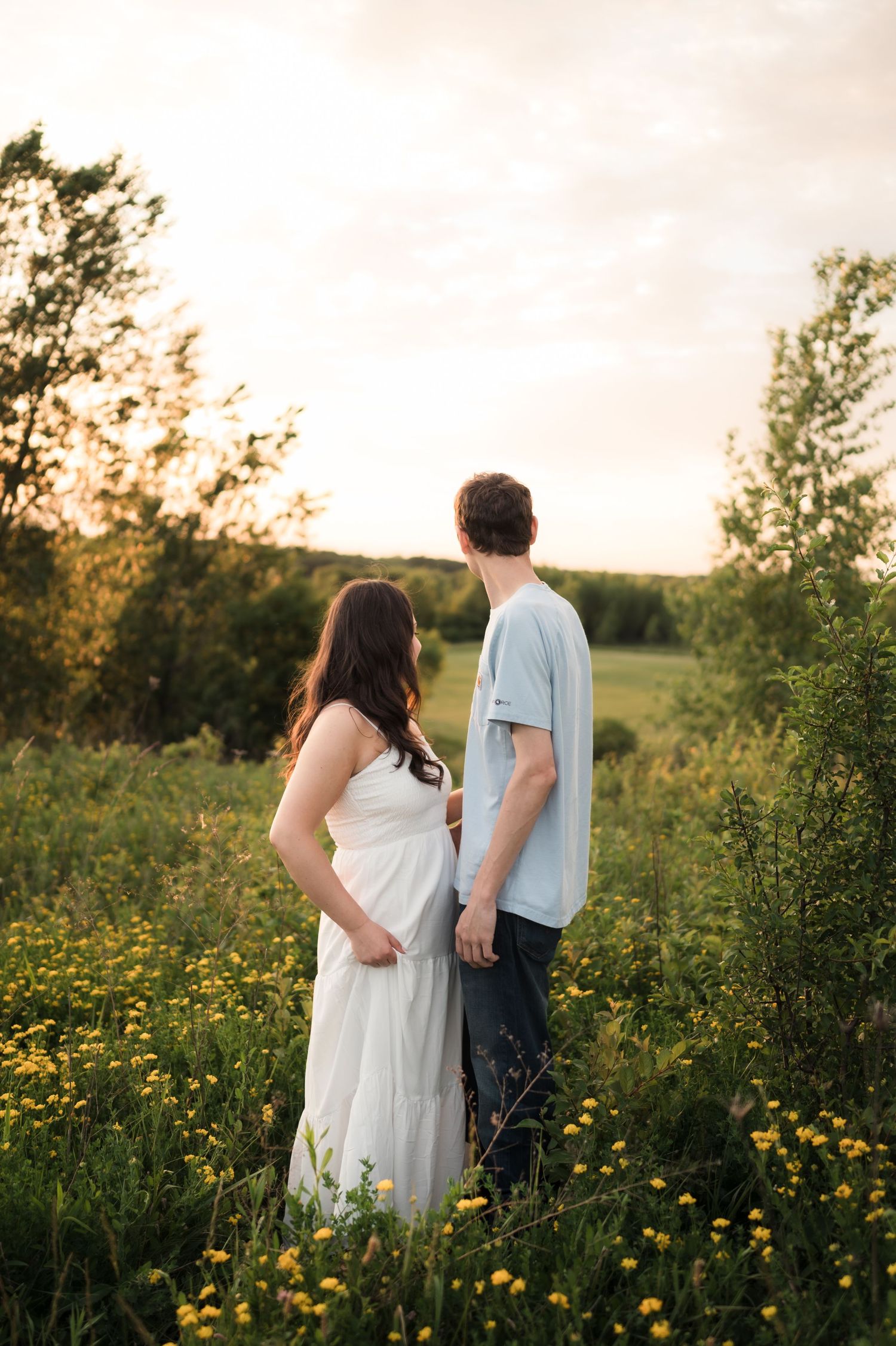 Couple standing hand in hand in a wildflower meadow with yellow blooms at a glowing sunset.
