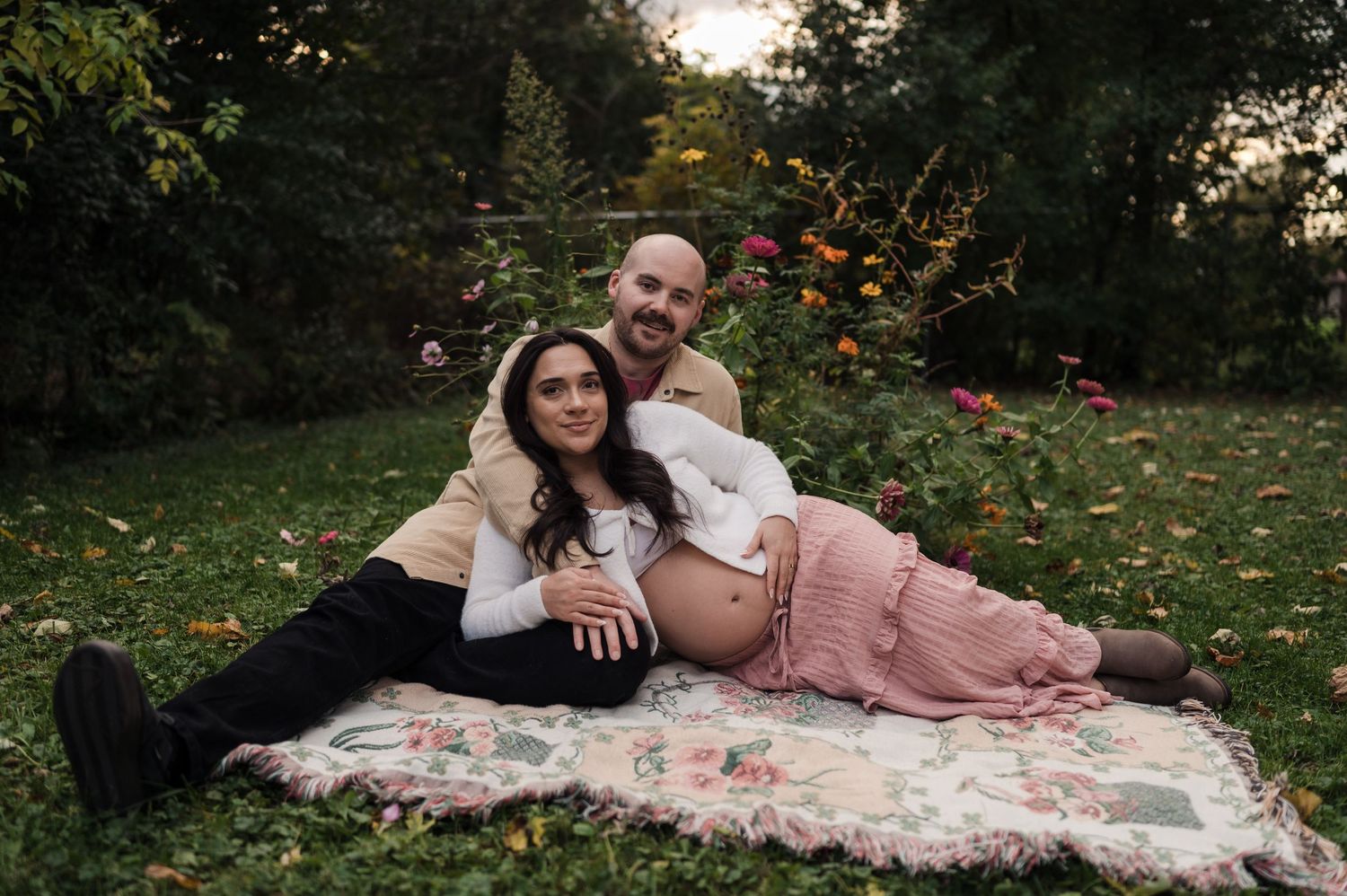 Expecting couple relaxing on a floral blanket in a garden surrounded by autumn foliage.